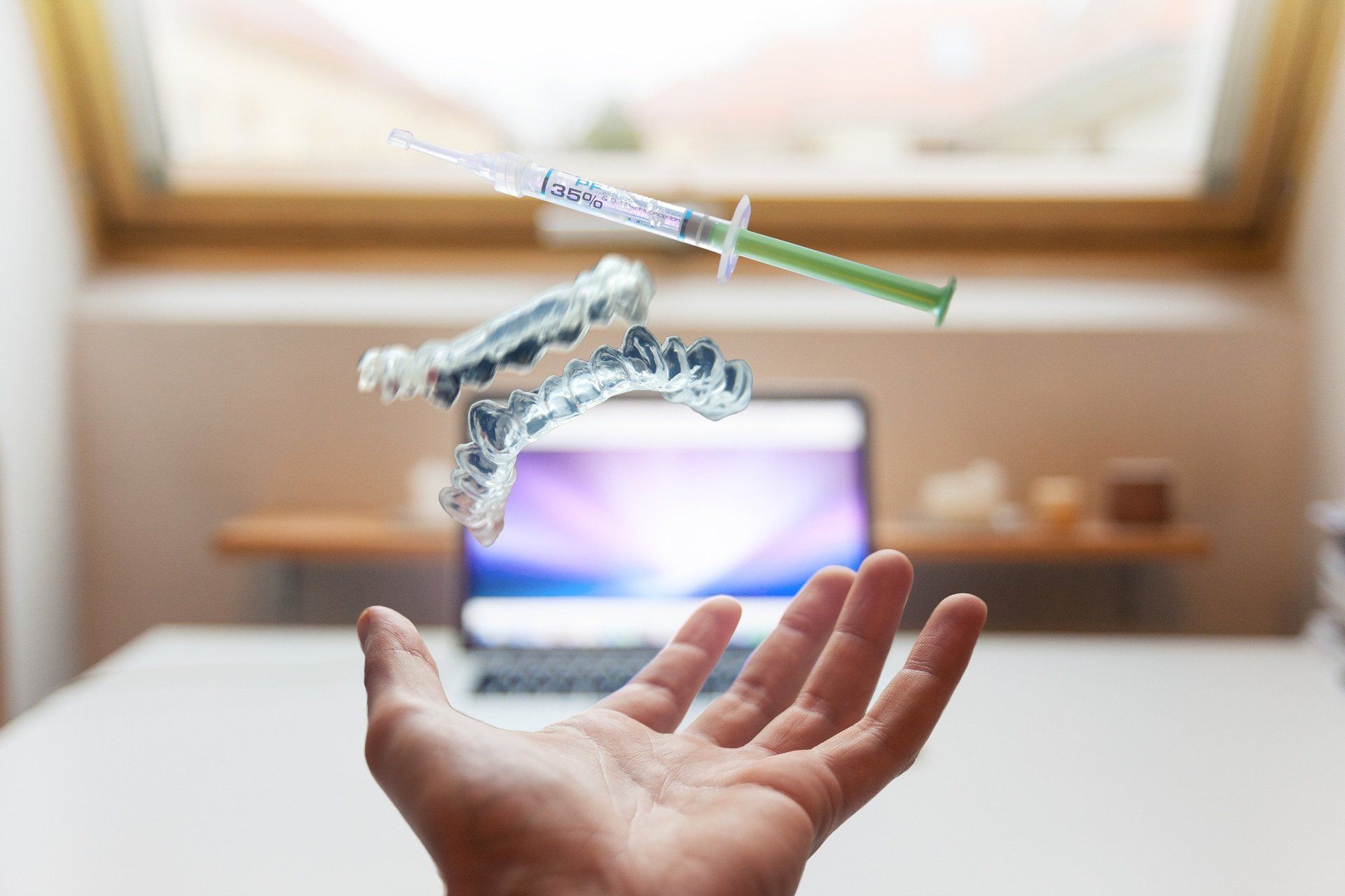 A person is holding a syringe and teeth whitening trays in their hand.