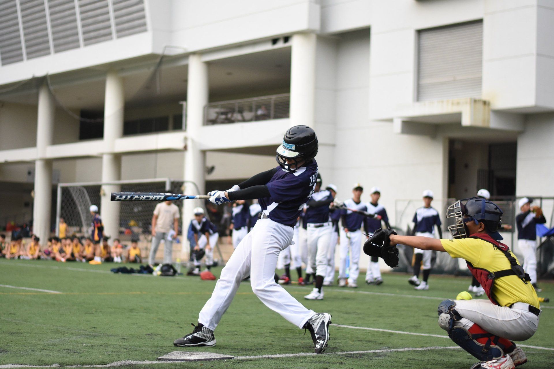 A baseball player is swinging a bat at a ball while a catcher watches.