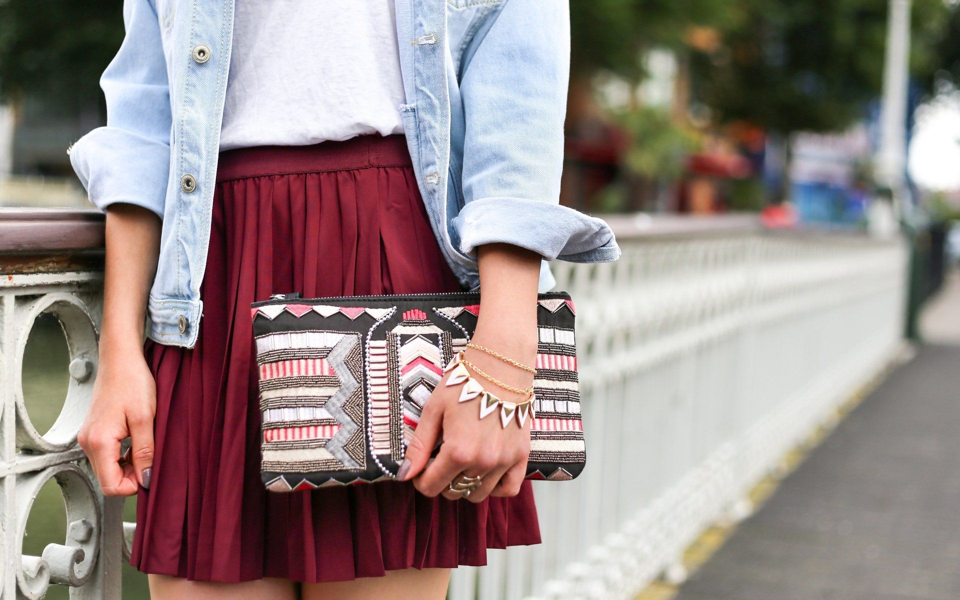 Una donna che indossa una gonna rossa e una giacca di jeans tiene in mano una pochette.