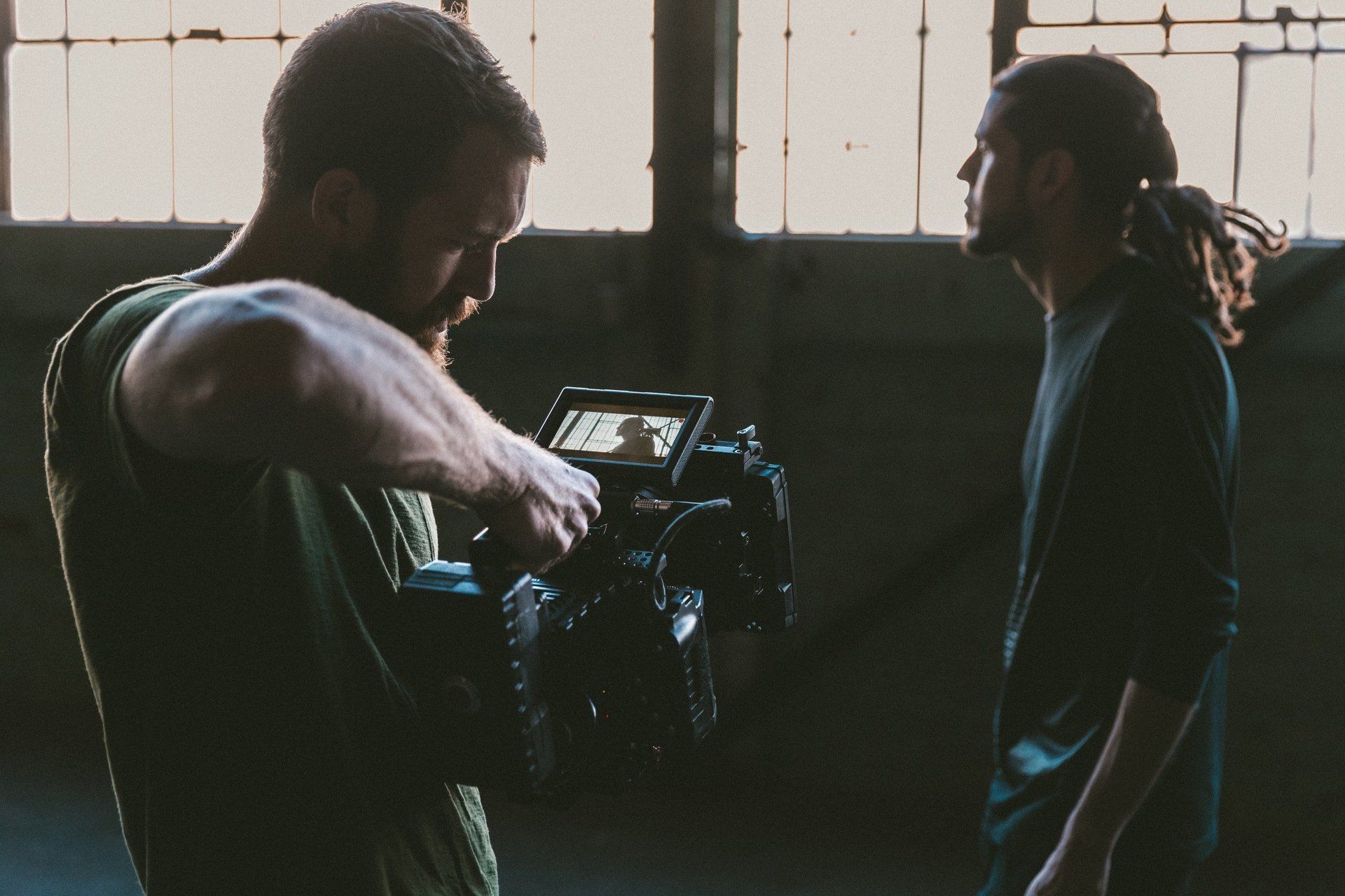 Two men are standing in front of a camera in a dark room.
