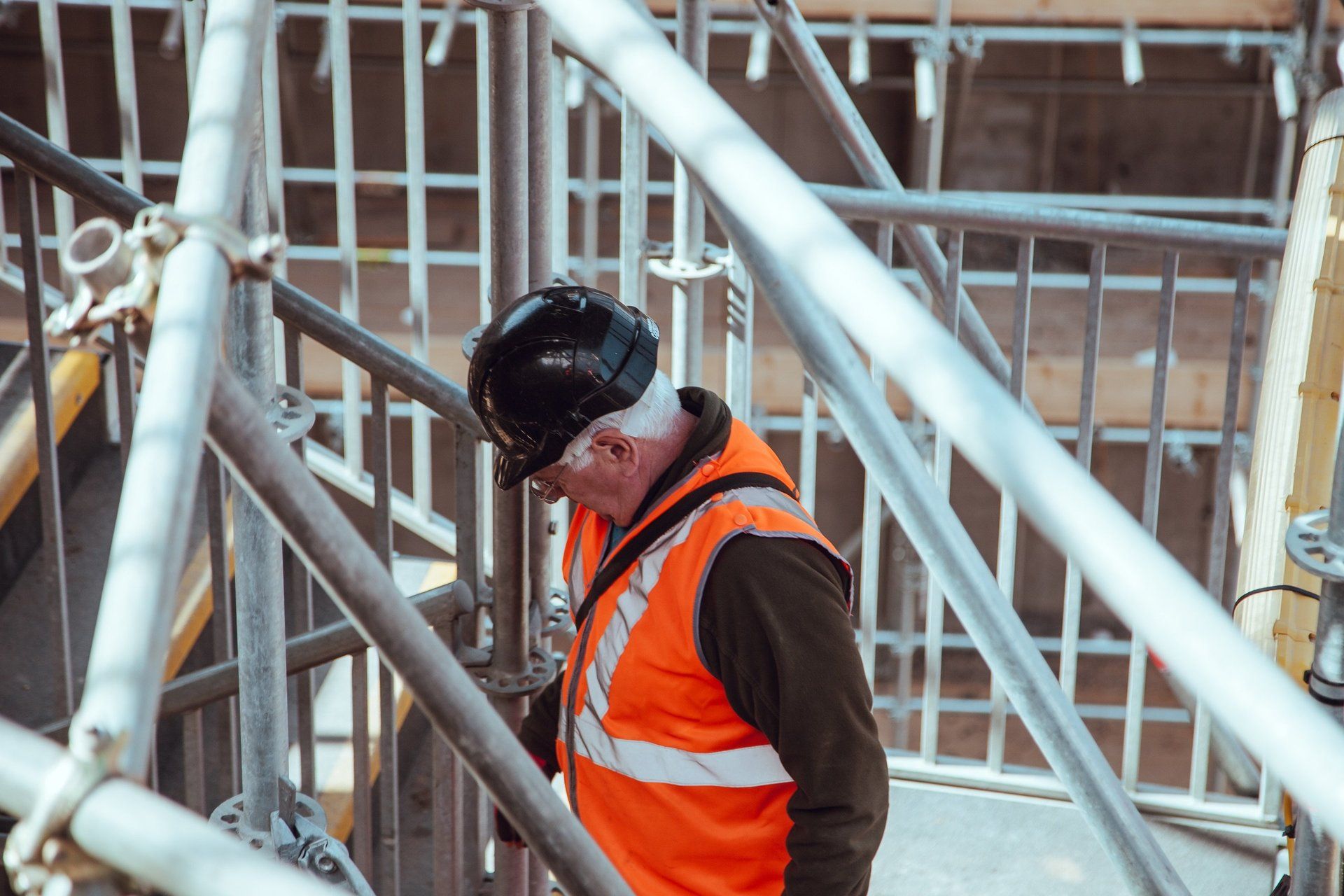 A man wearing a hard hat and an orange vest is standing on a scaffolding.