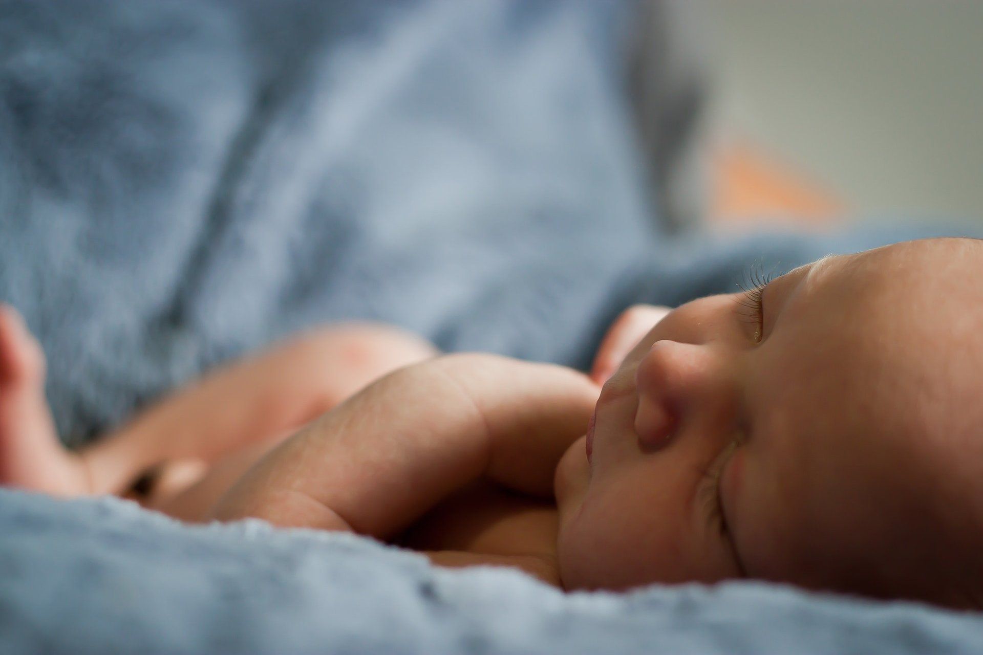 A newborn baby is sleeping on a blue blanket.