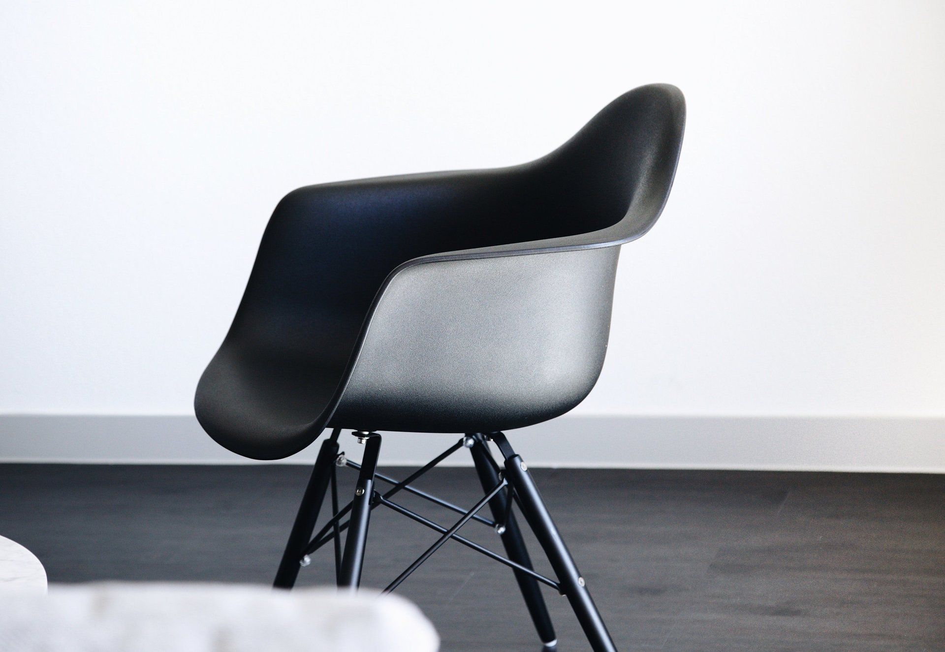 Una poltrona nera in stile Eames con seduta sagomata e base in filo metallico nero, posizionata su una parete bianca su un pavimento scuro.