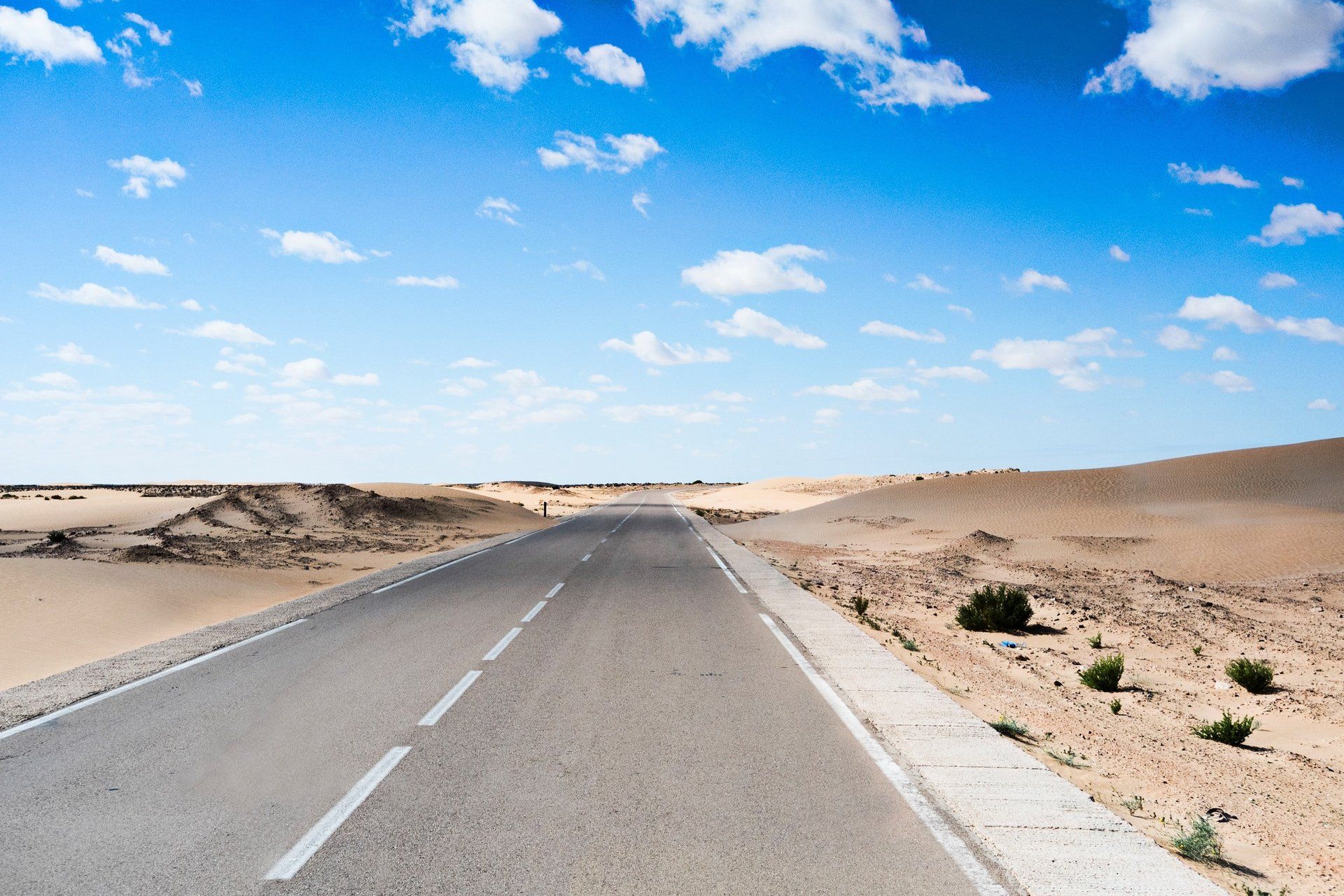 An empty road in the desert with a blue sky in the background