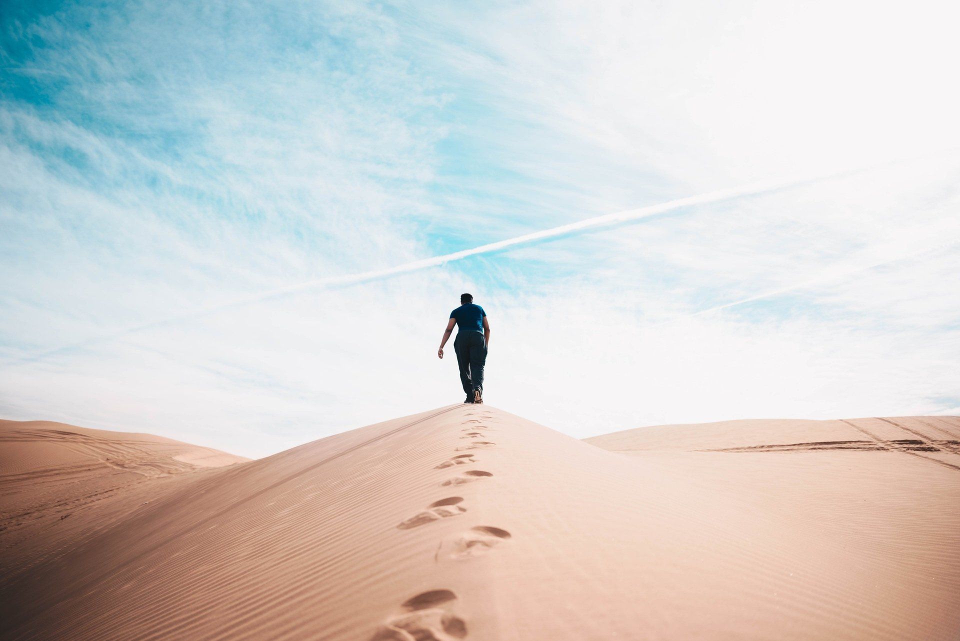 A man is walking up a sand dune in the desert.