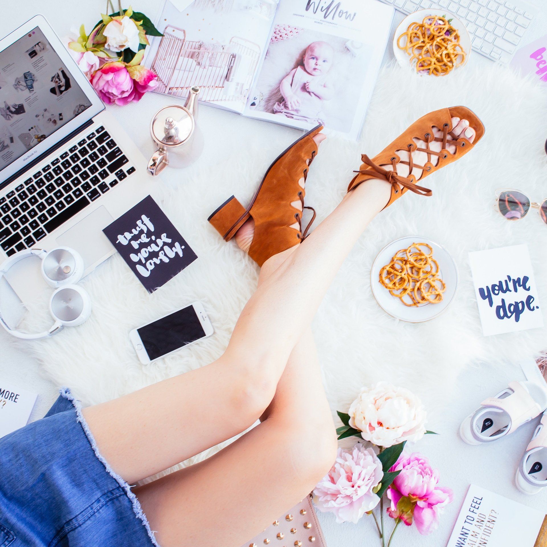 A woman is laying on the floor with her legs crossed in front of a laptop and a sign that says you 're dope