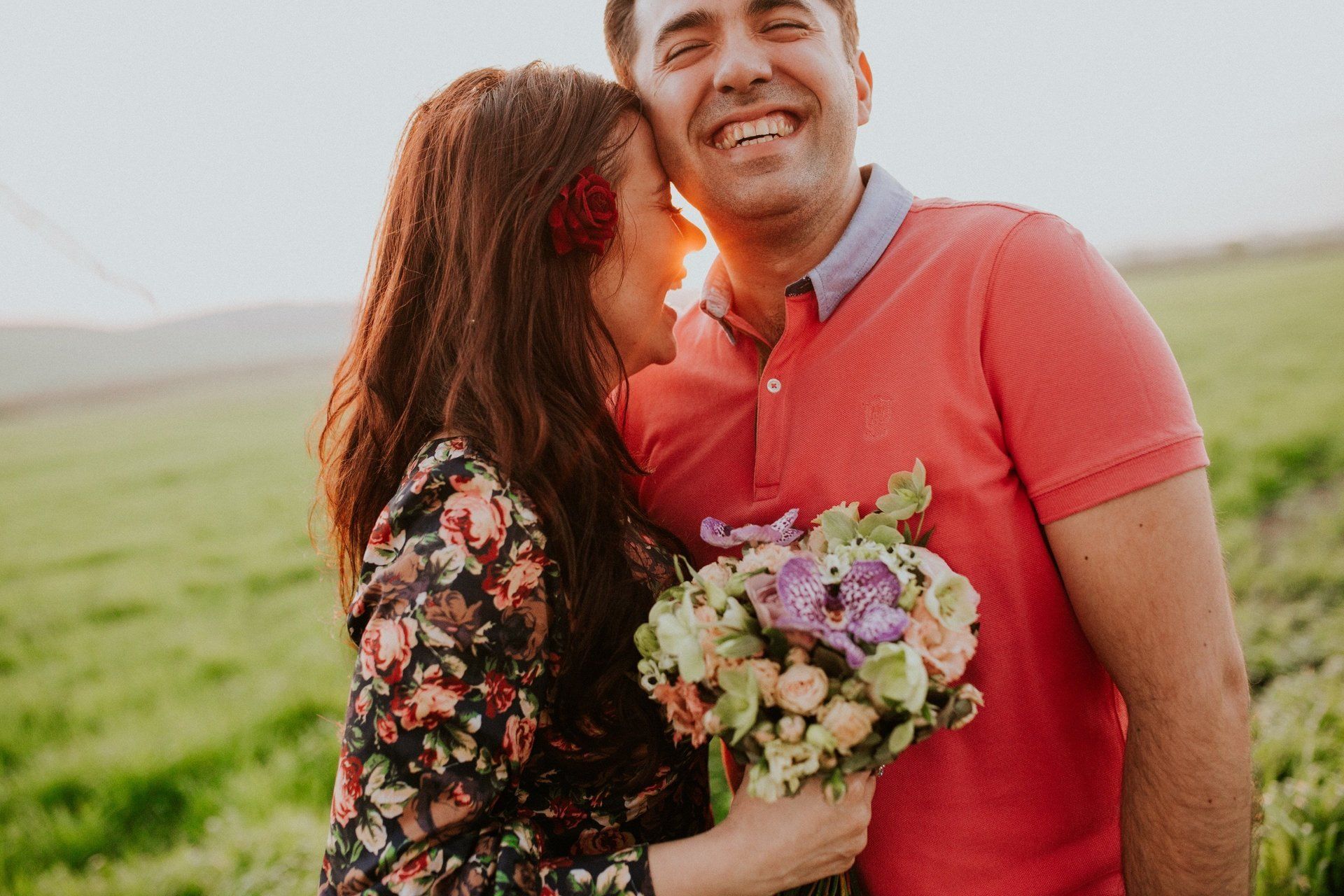 A woman is kissing a man on the cheek while holding a bouquet of flowers.