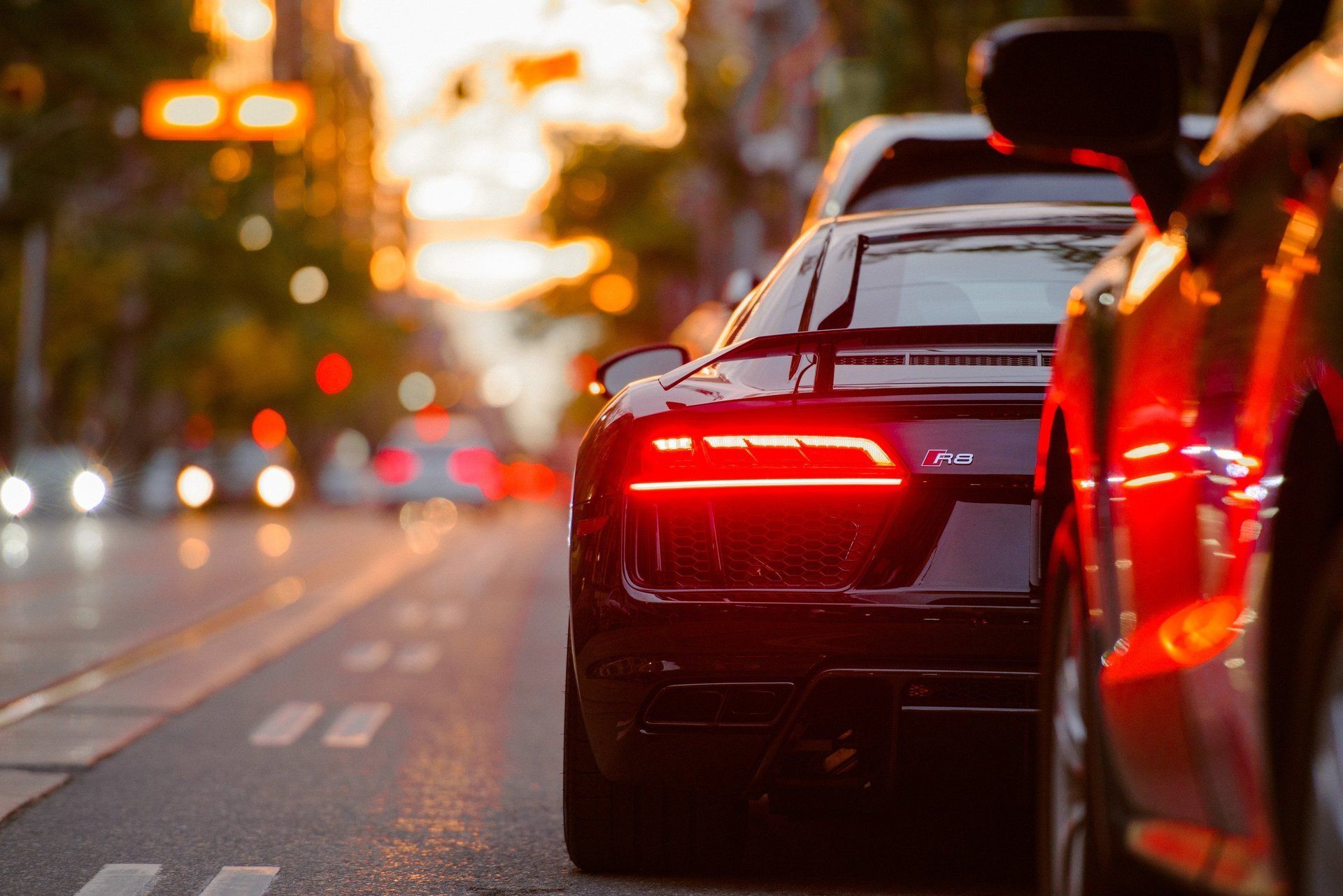 Black car with red tail lights on a city street at sunset, traffic in the distance.