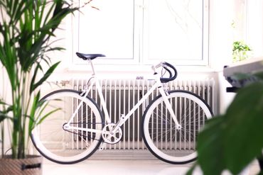 A white bicycle is parked on a radiator next to a window.