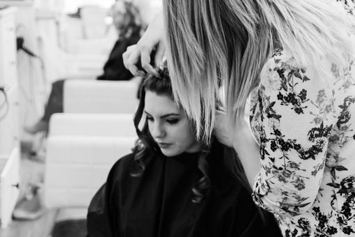 A stylist curling a customer's hair in a salon; black and white.