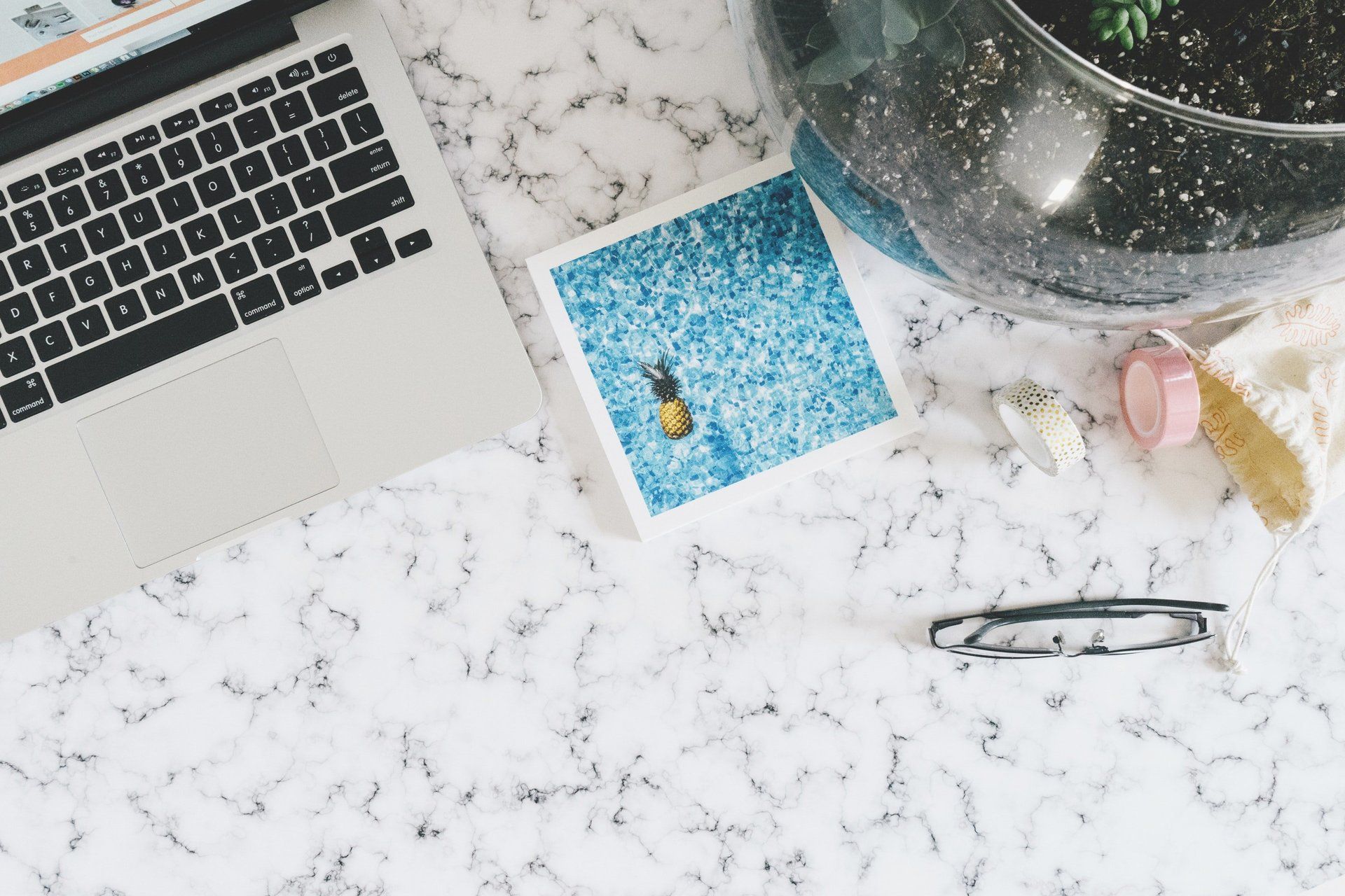 A laptop computer is sitting on a marble table next to a picture of a pineapple.