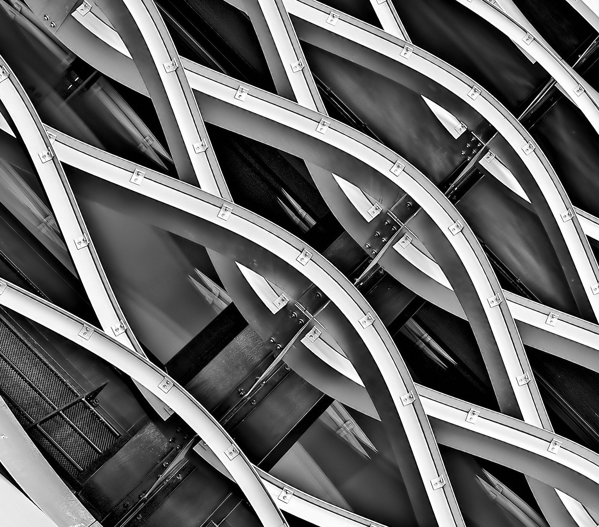 Una veduta astratta in bianco e nero ad alto contrasto di travi d'acciaio curve e intersecanti su una grande struttura di ponte moderna.