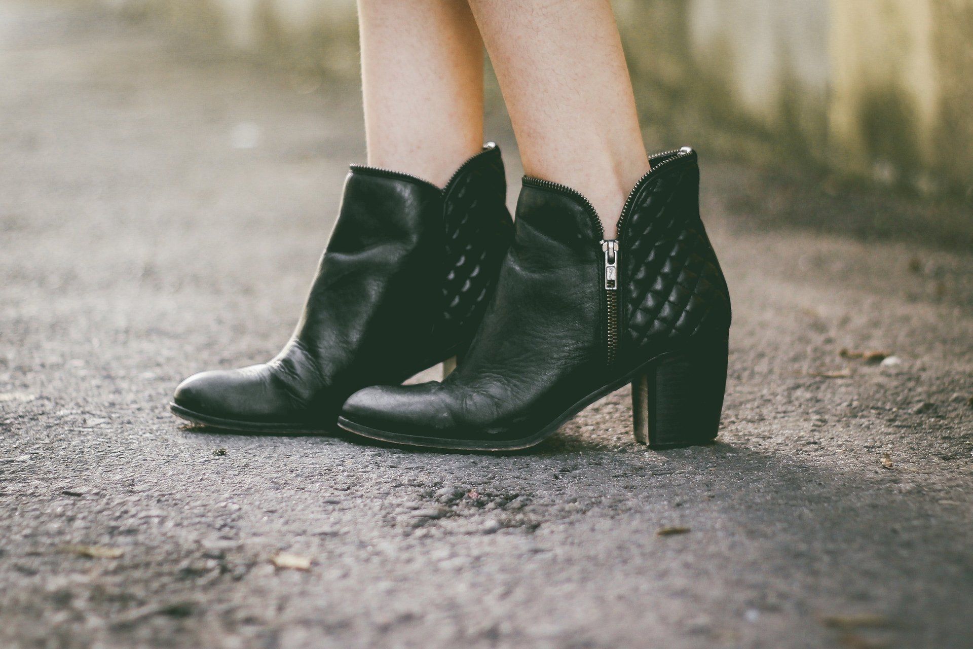 A woman stands in high-heeled black booties on asphalt. A woman stands in black booties on asphalt in West Chester, Ohio.