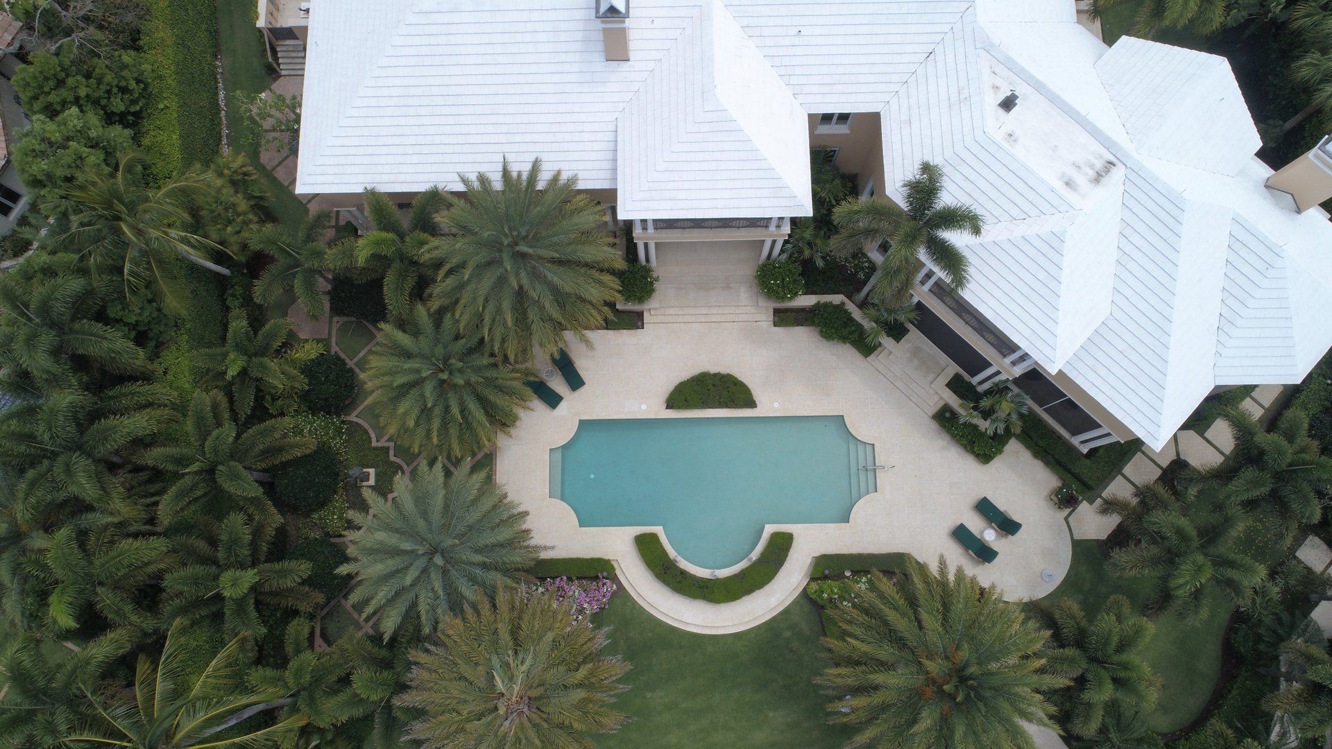 An aerial view of a large house with a swimming pool surrounded by palm trees.