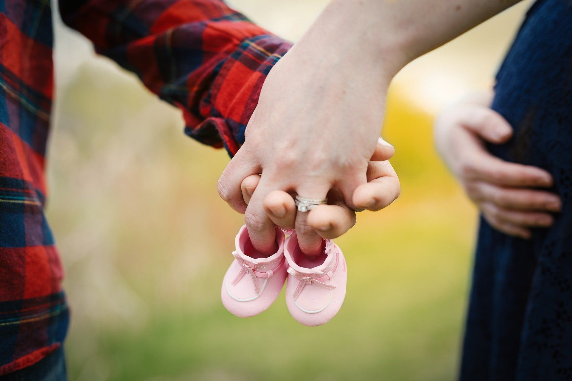 Een stel houdt elkaars handen vast, met roze babyschoentjes ertussen