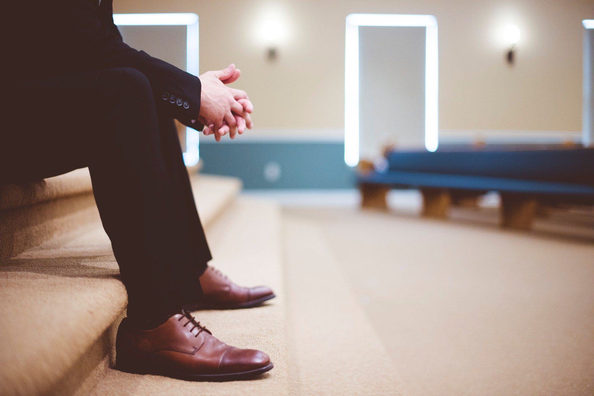 Person seated on a church pew, hands clasped, in a softly lit sanctuary