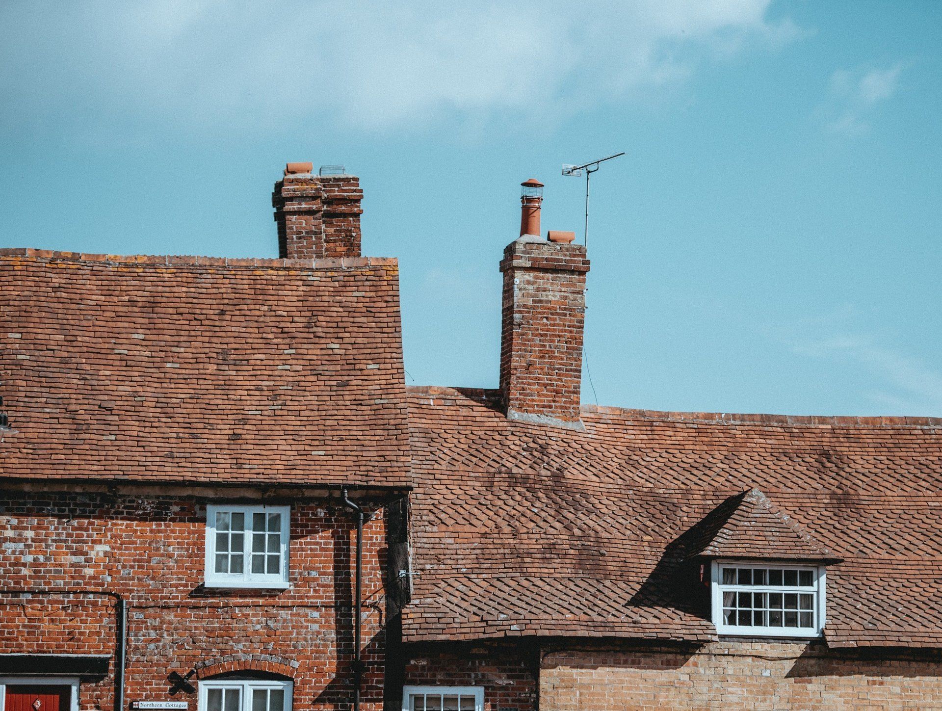 Brick buildings with tiled roofs and chimneys against a blue sky.