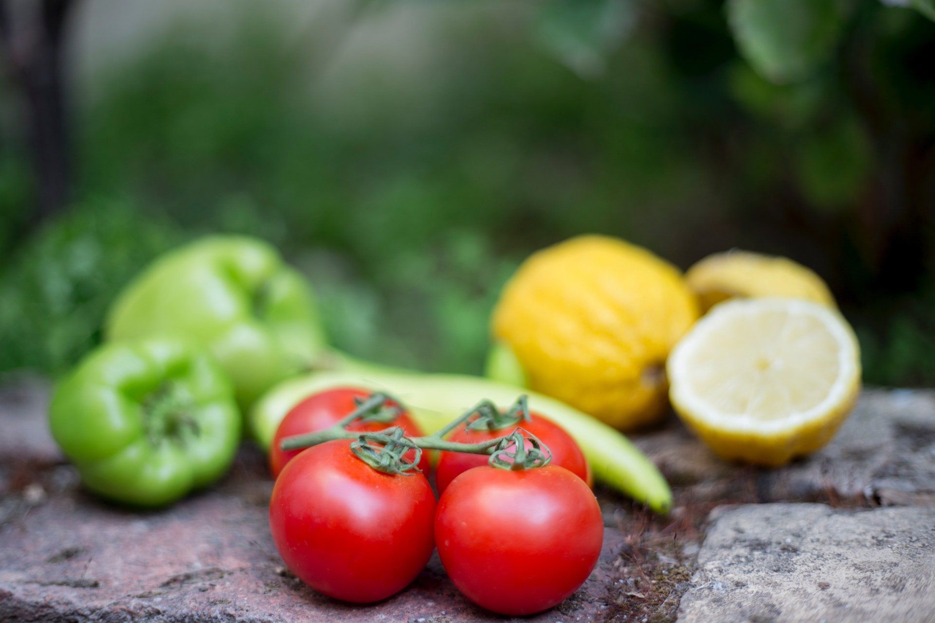 Tomatoes , peppers , lemons and cucumbers are sitting on a rock.