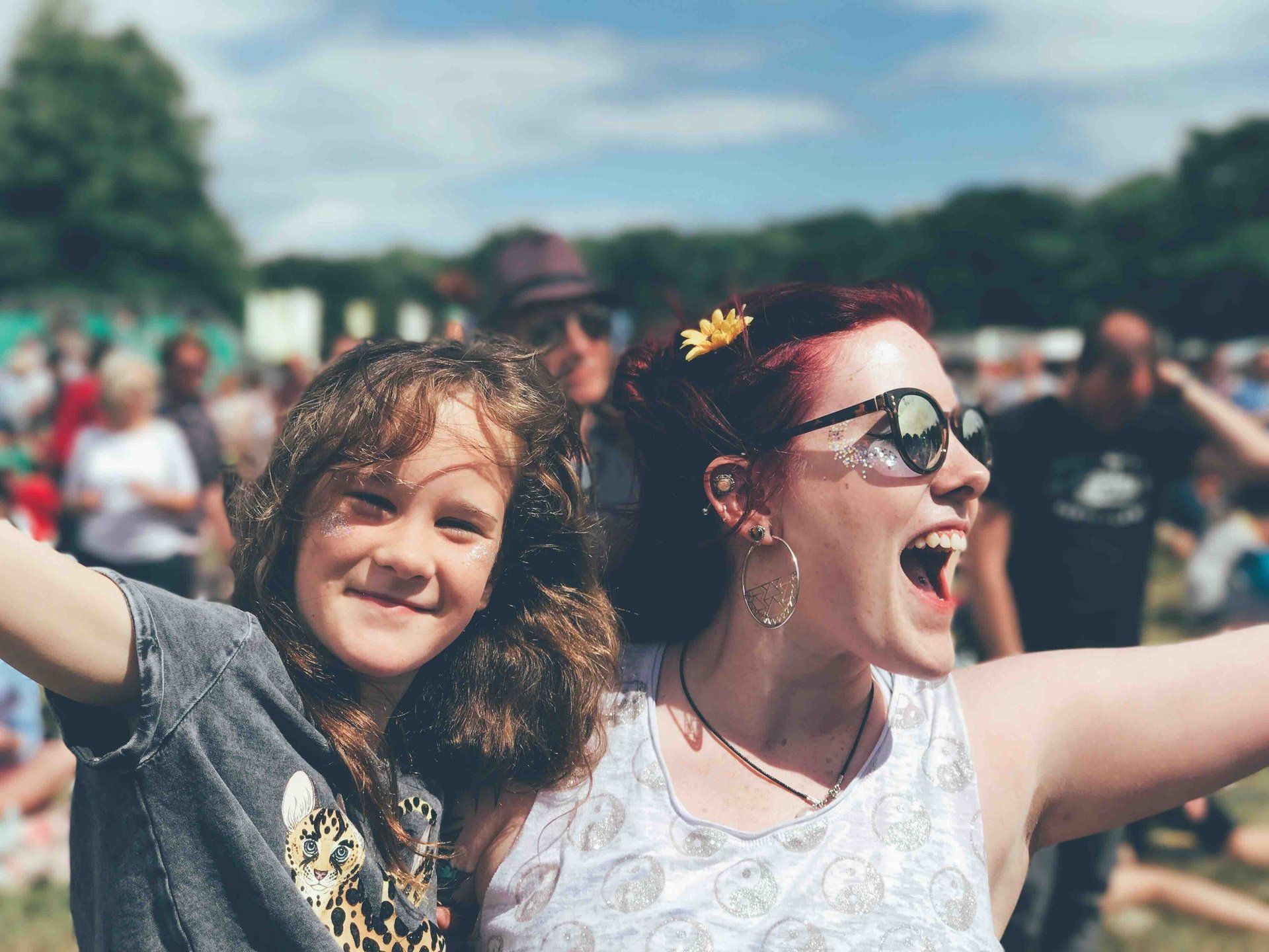 A woman and a little girl are standing next to each other at a music festival.