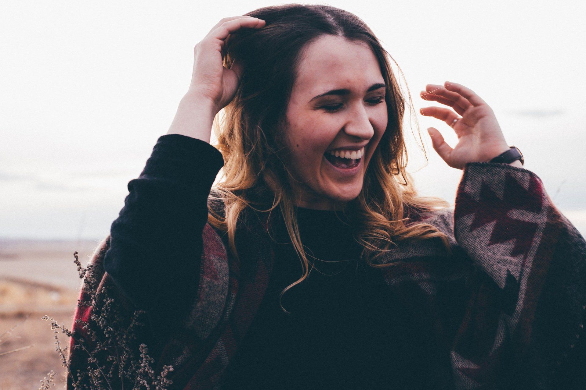 Smiling woman outdoors, laughing with hands in her hair on a beach