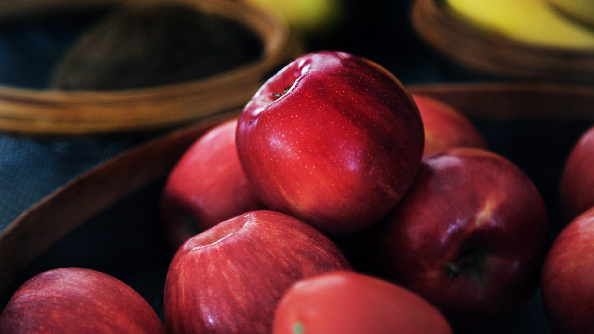 Red apples stacked in a bowl, with a glossy apple centered in the foreground
