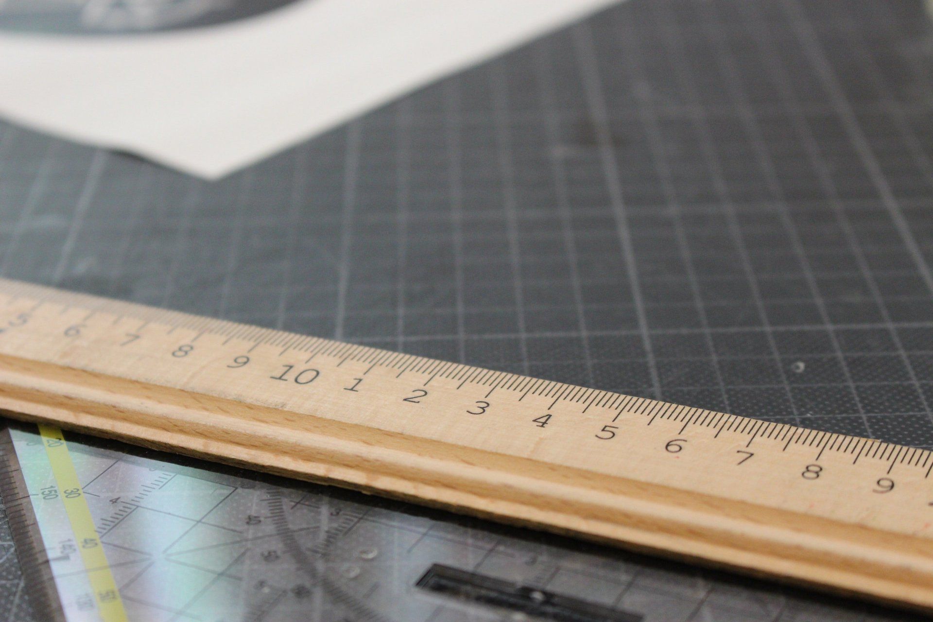 Wooden ruler on a gray cutting mat, partially obscuring a map, paper in the background.