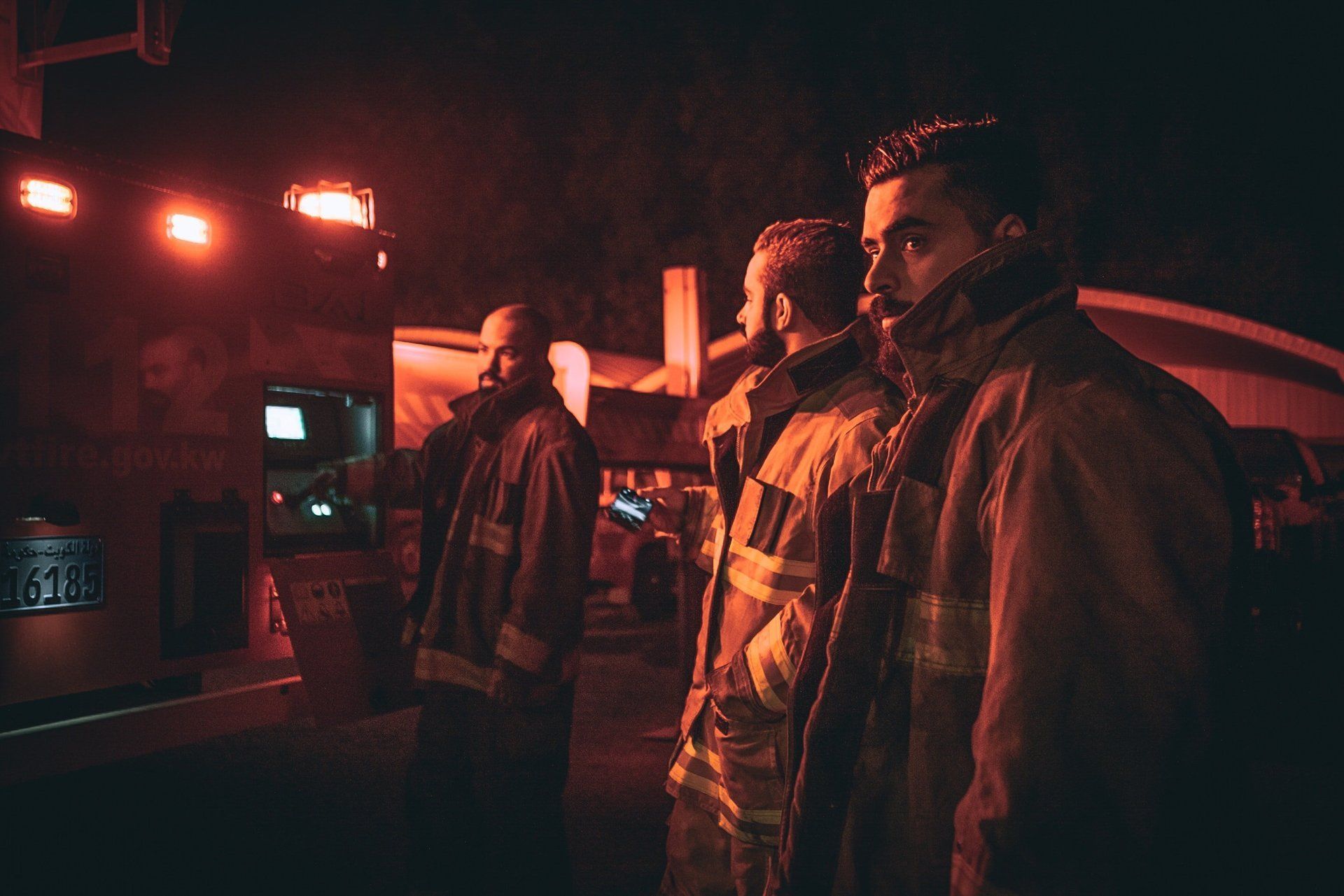 A group of firefighters are standing next to each other in front of an ambulance at night.