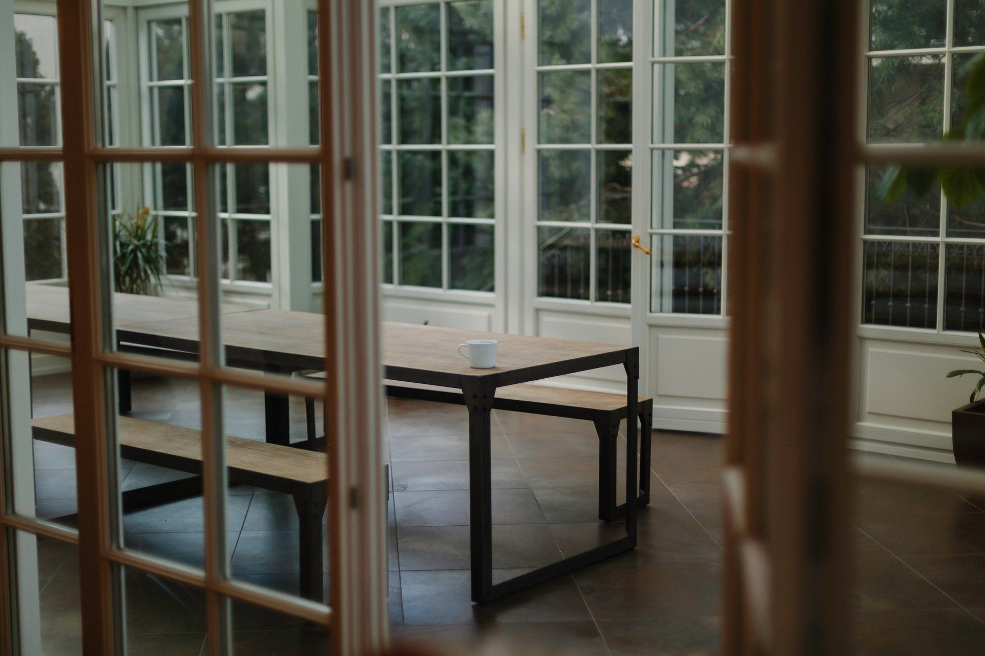 A room with a table and benches in it and a lot of windows.