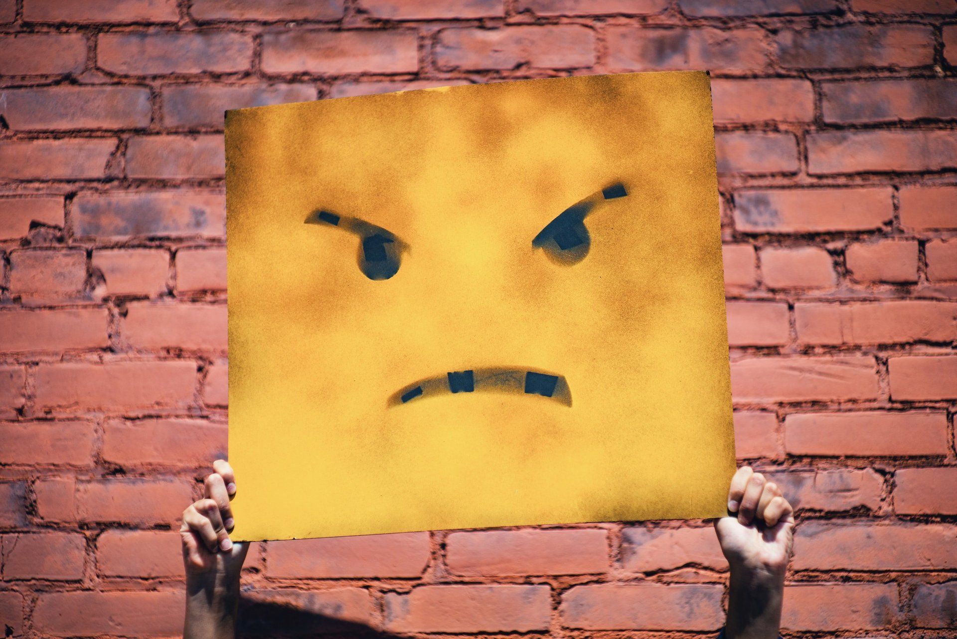 A person is holding a piece of paper with an angry face drawn on it.