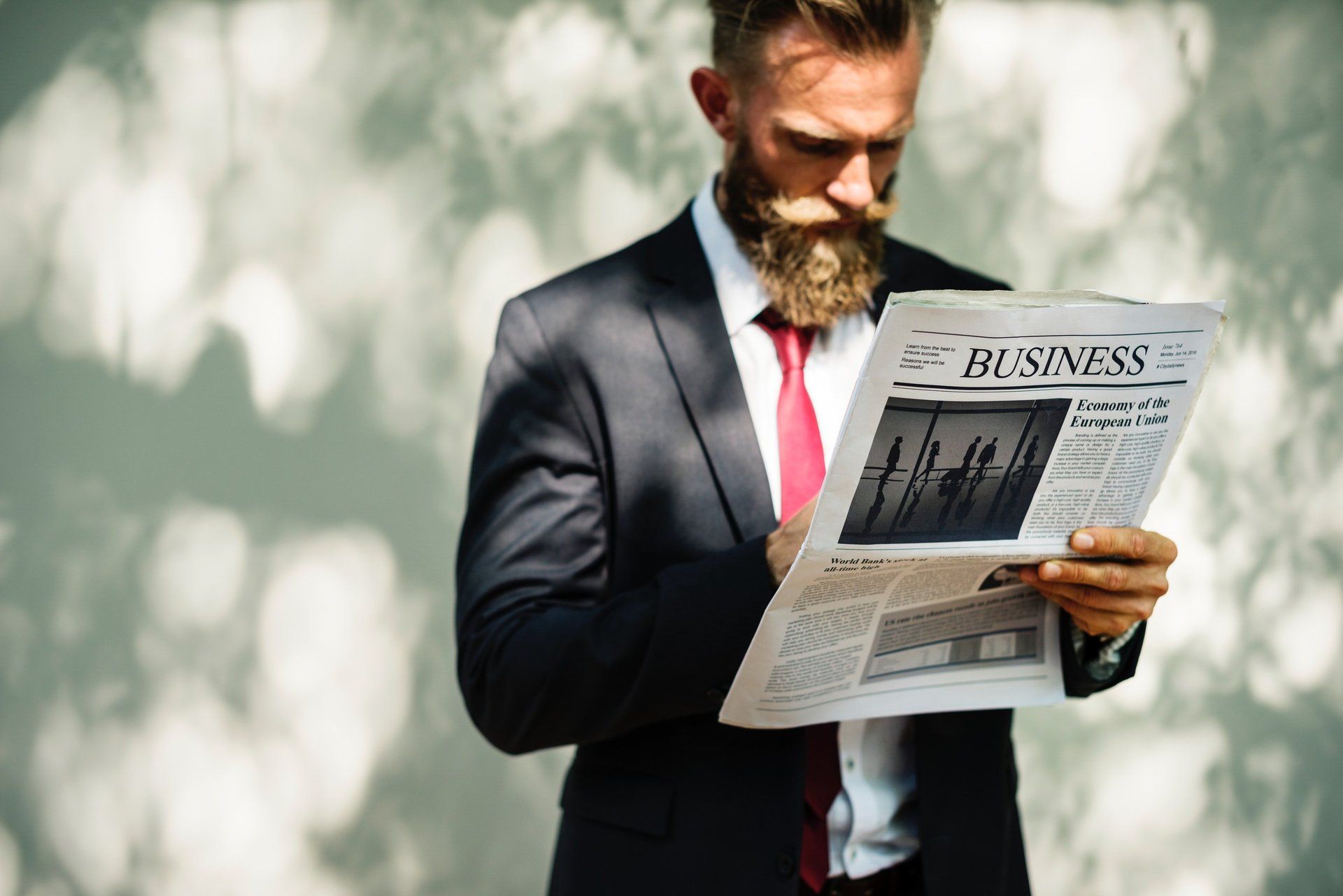Hombre de traje con corbata roja leyendo el periódico comercial.