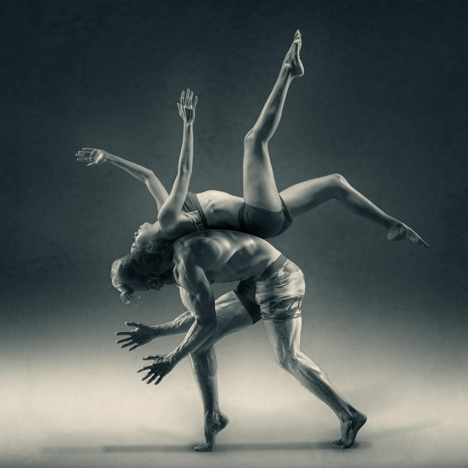 Una foto in bianco e nero scattata in studio che ritrae due ballerini in una complessa posa acrobatica di sollevamento, su uno sfondo scuro.