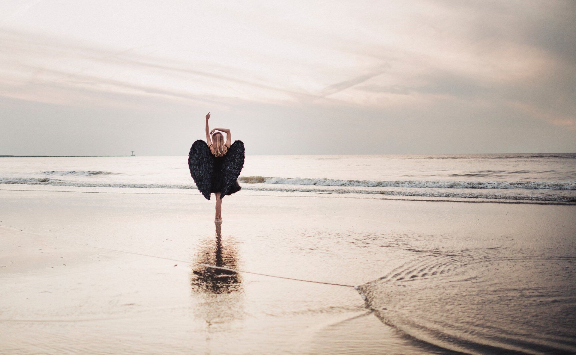A woman in a black dress is dancing on the beach.