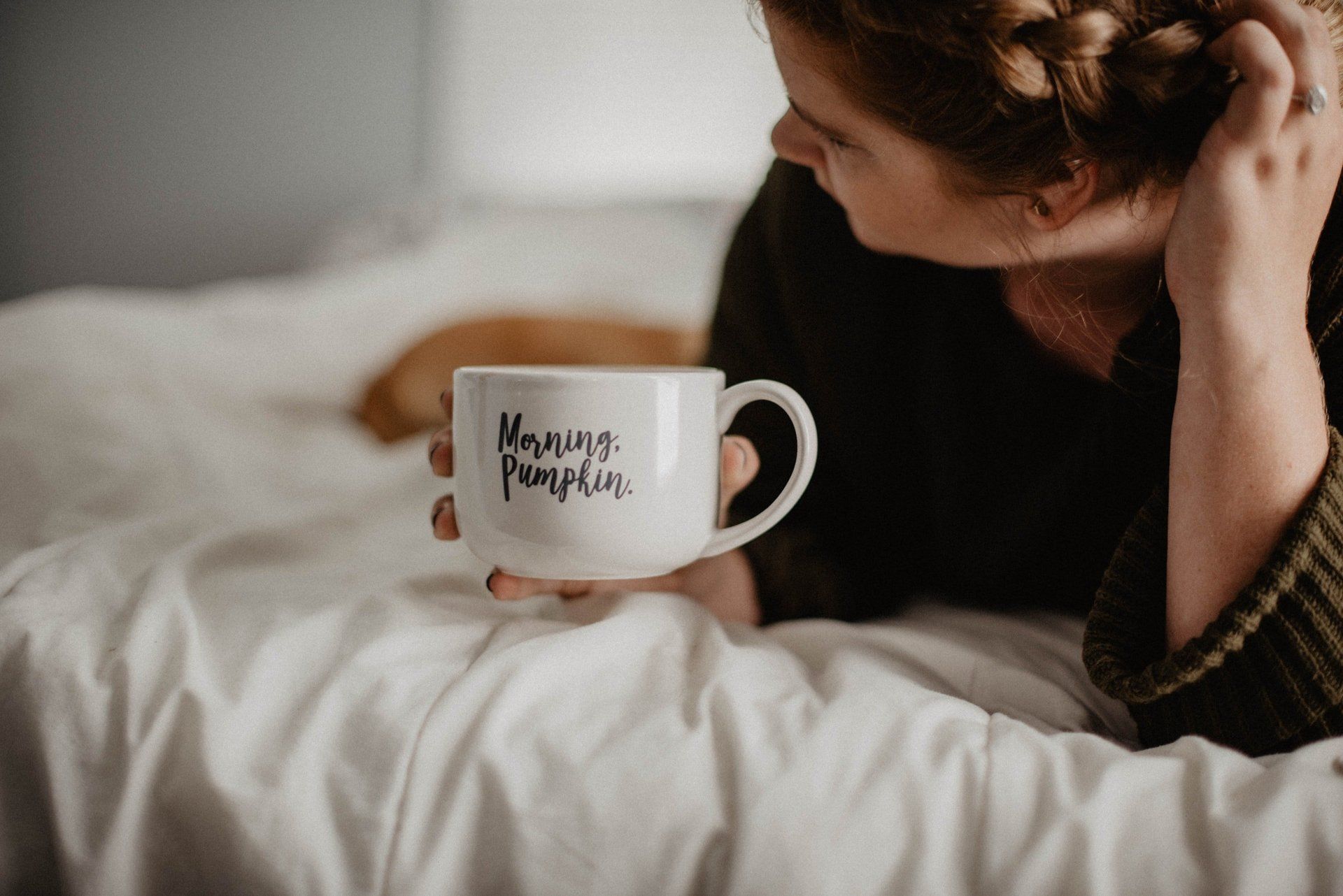 Una donna sdraiata sul letto con in mano una tazza di caffè