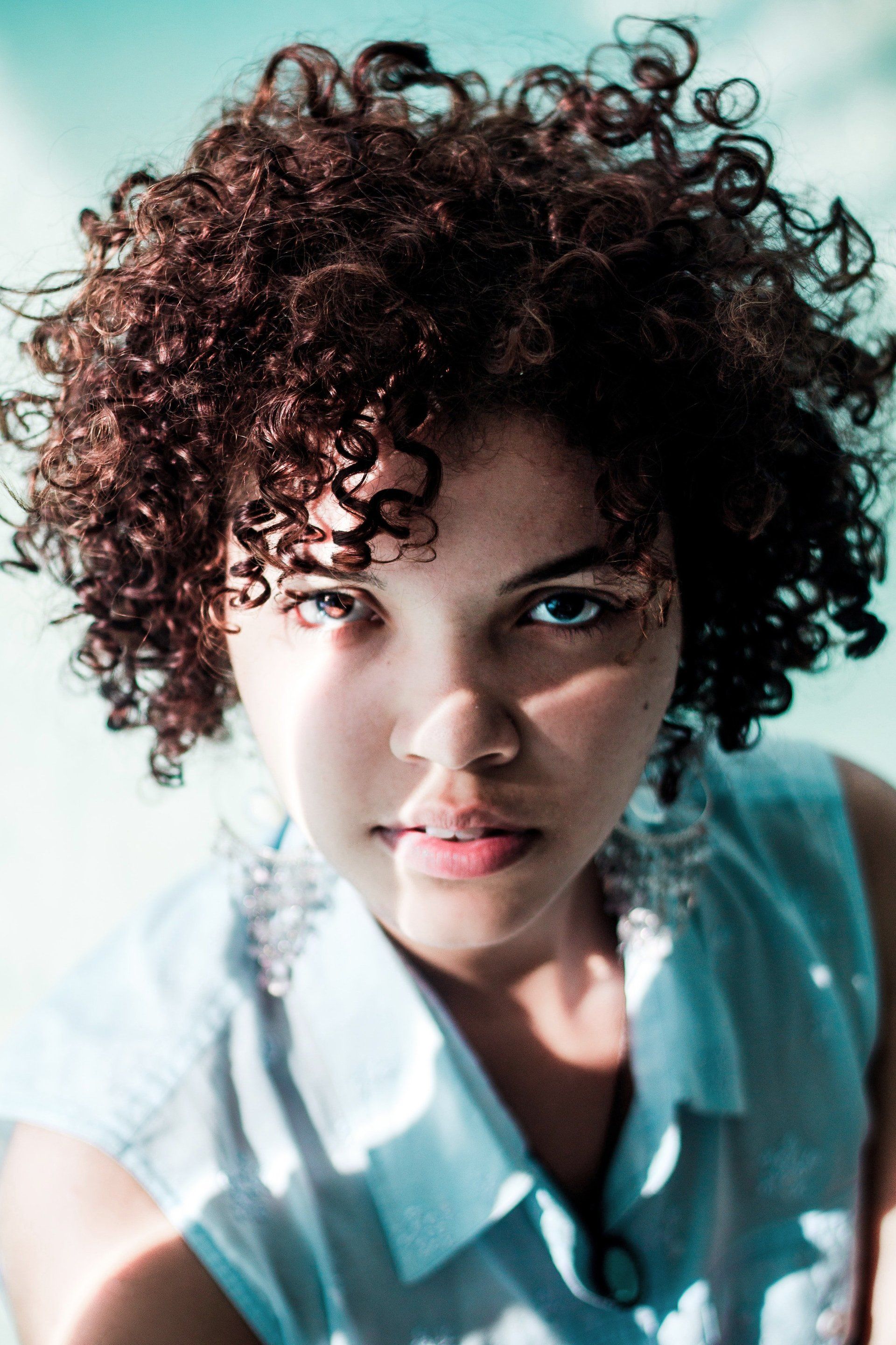 A young woman with curly hair looks at the camera.