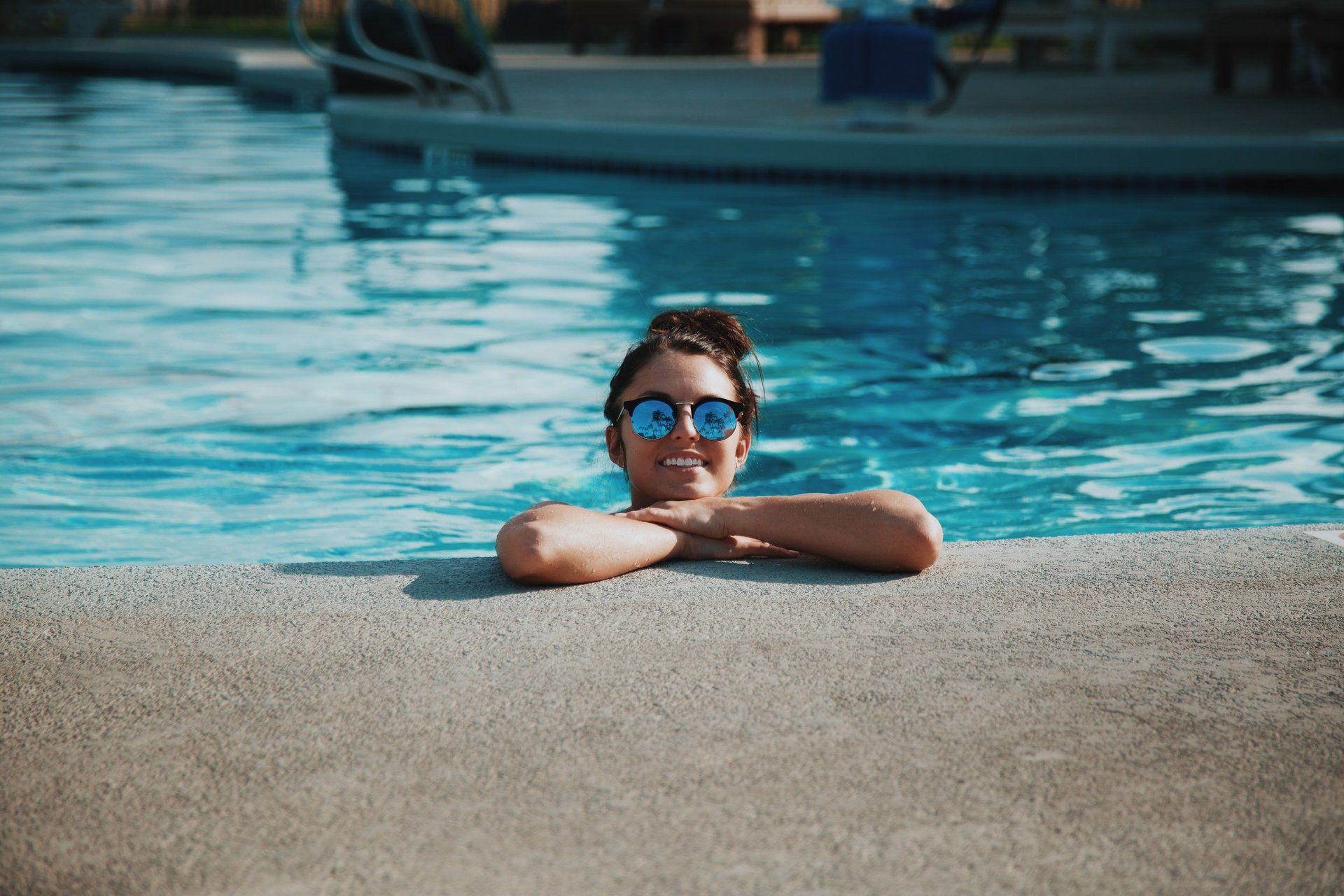 Person resting at the edge of a swimming pool, wearing blue goggles, with arms folded on the deck.