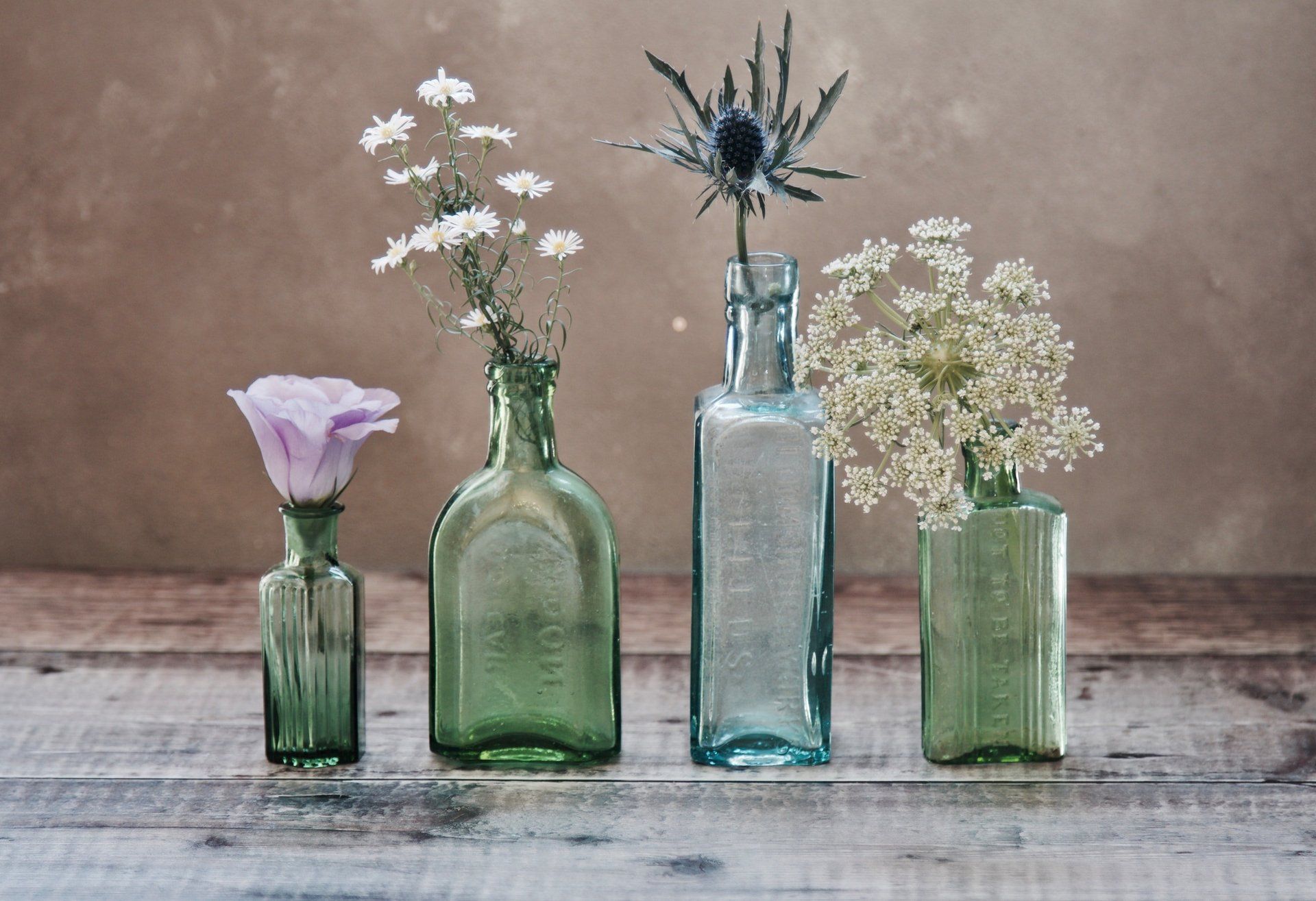 Four bottles filled with flowers are sitting on a wooden table.