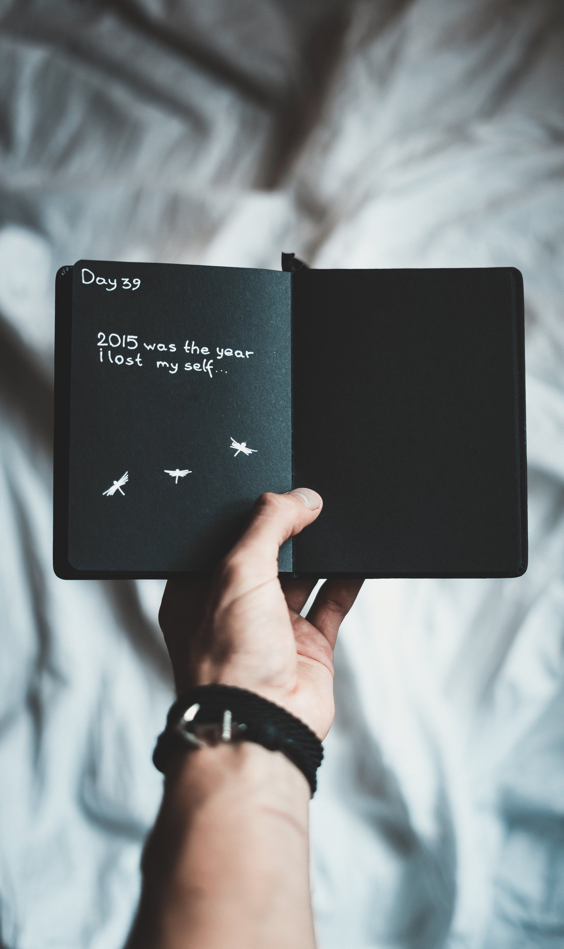 Hand holding open black notebook over bed, with handwritten notes on the left page.