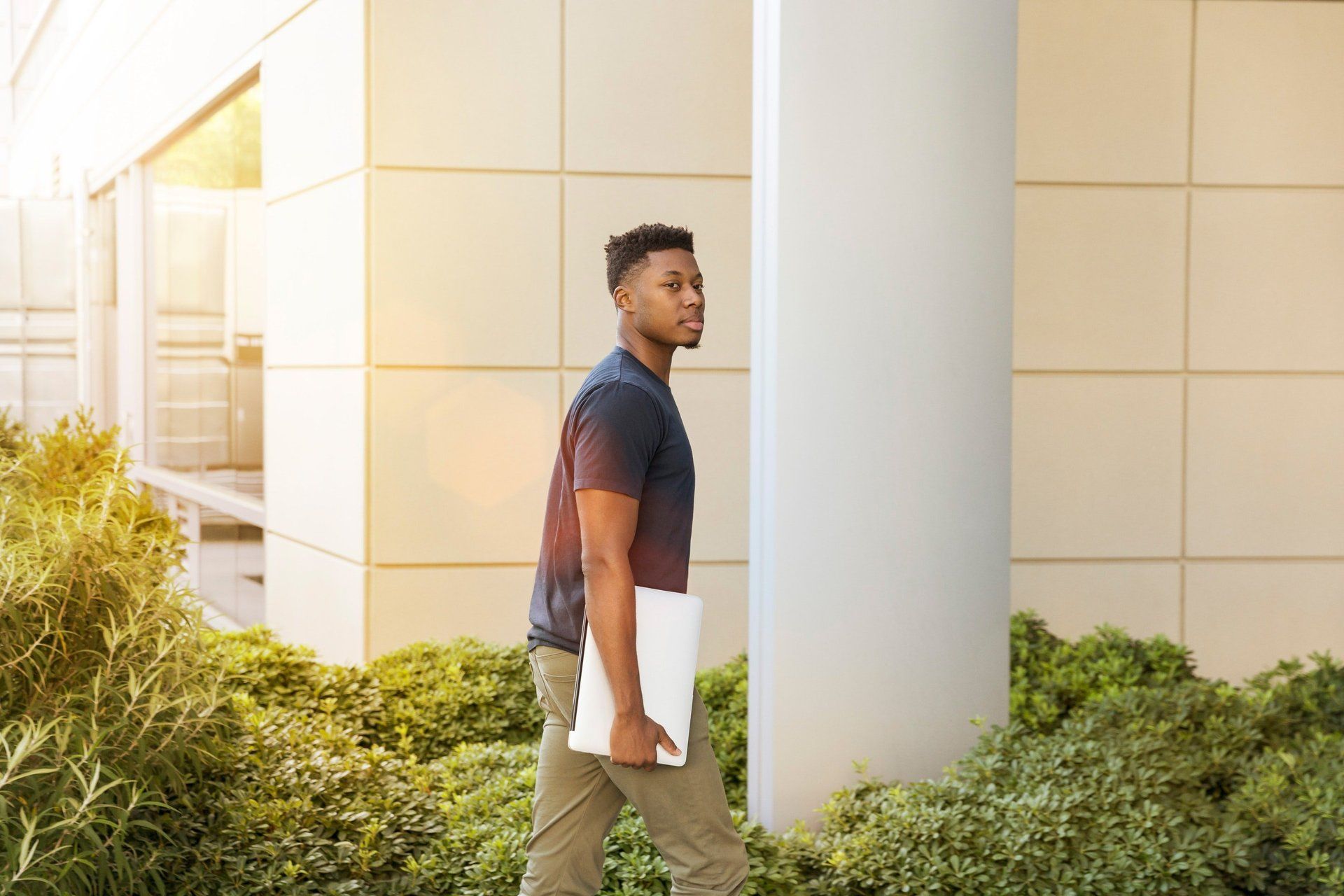A man is walking down a sidewalk holding a laptop.