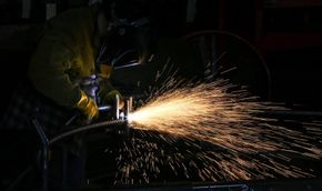 Worker welding metal in a dark workshop, sending a bright shower of sparks