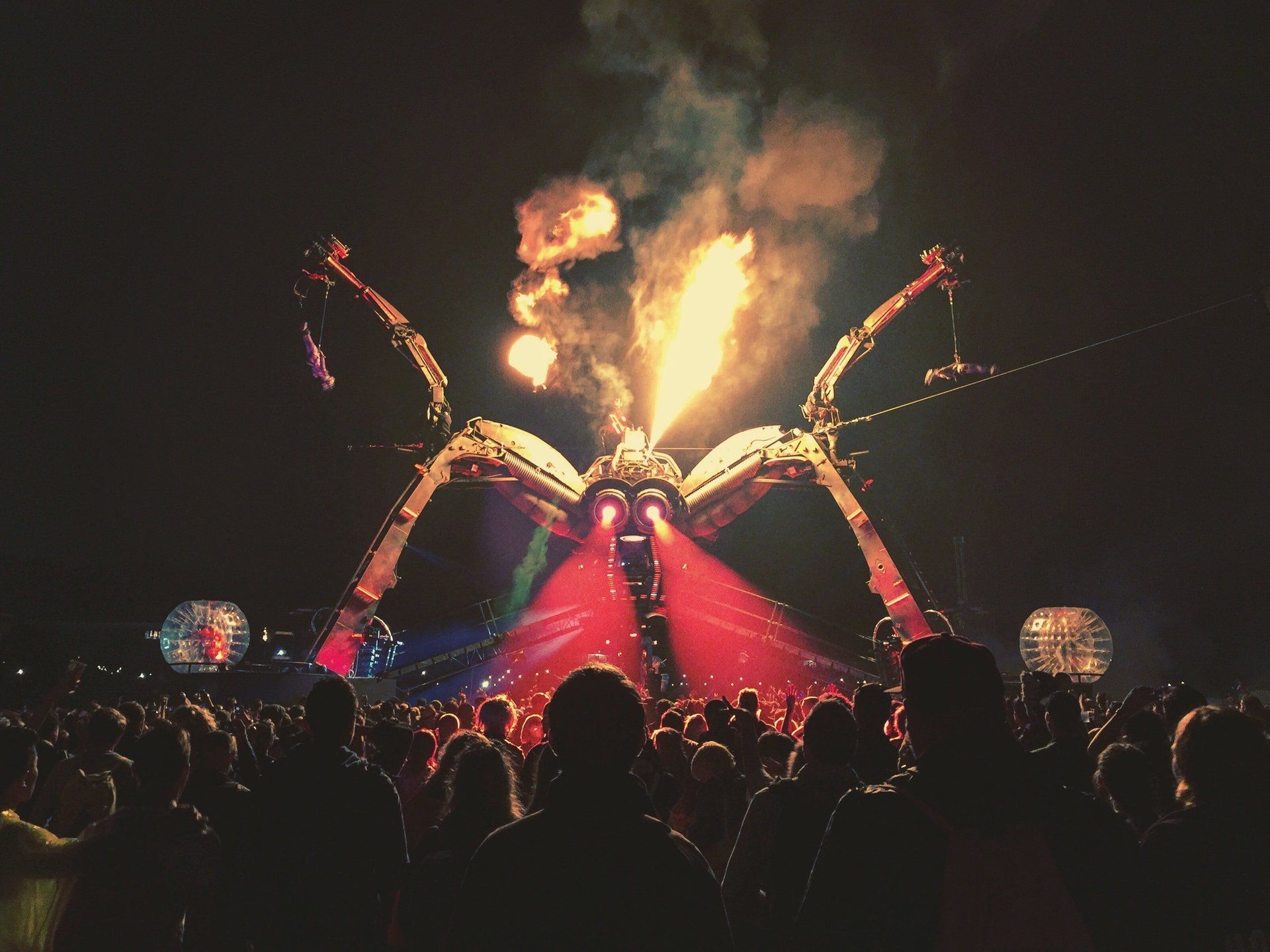 A crowd of people watching a giant spider with fire coming out of it 's mouth