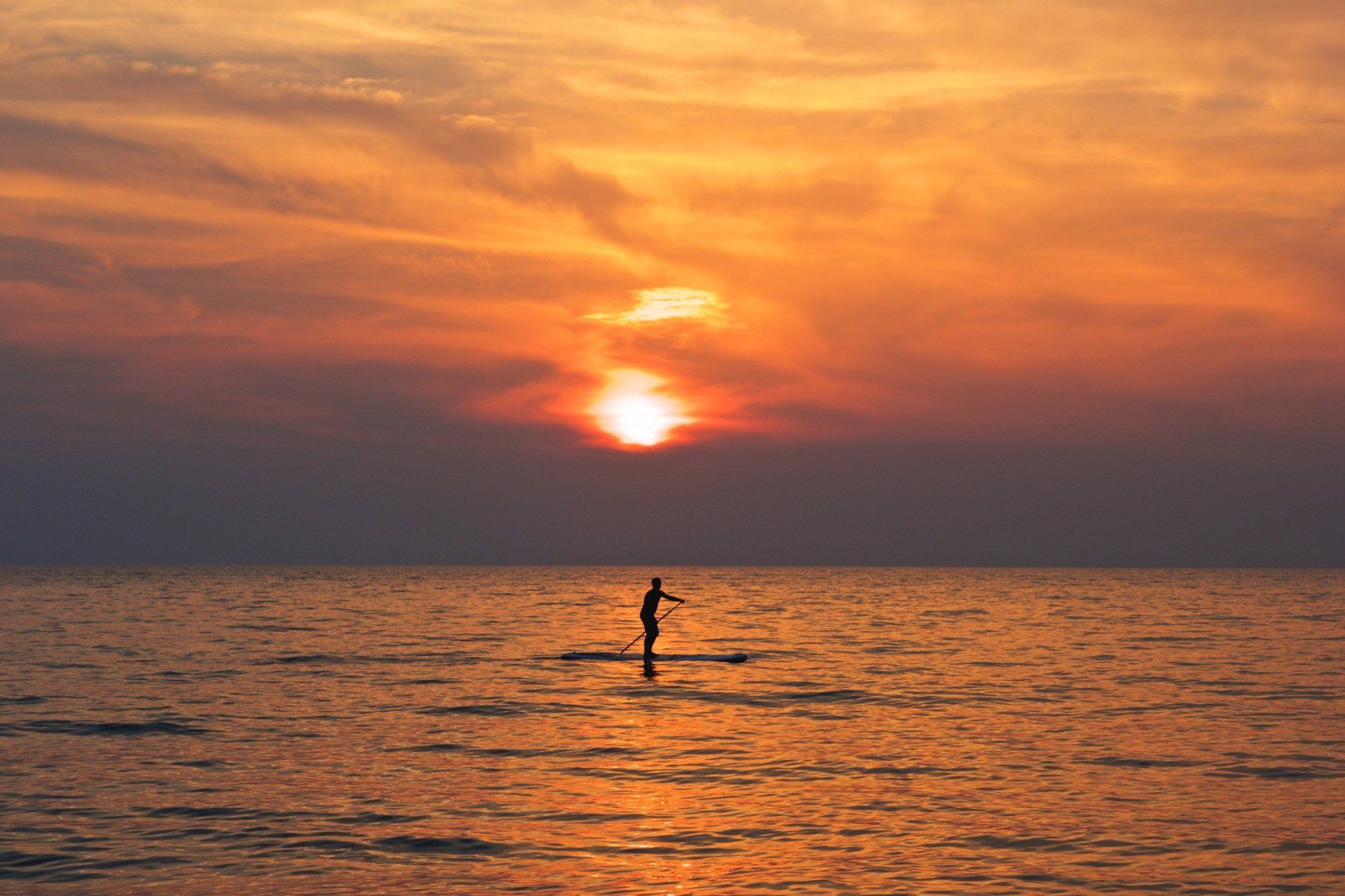 Una persona è in piedi su una tavola da paddle in mare al tramonto.