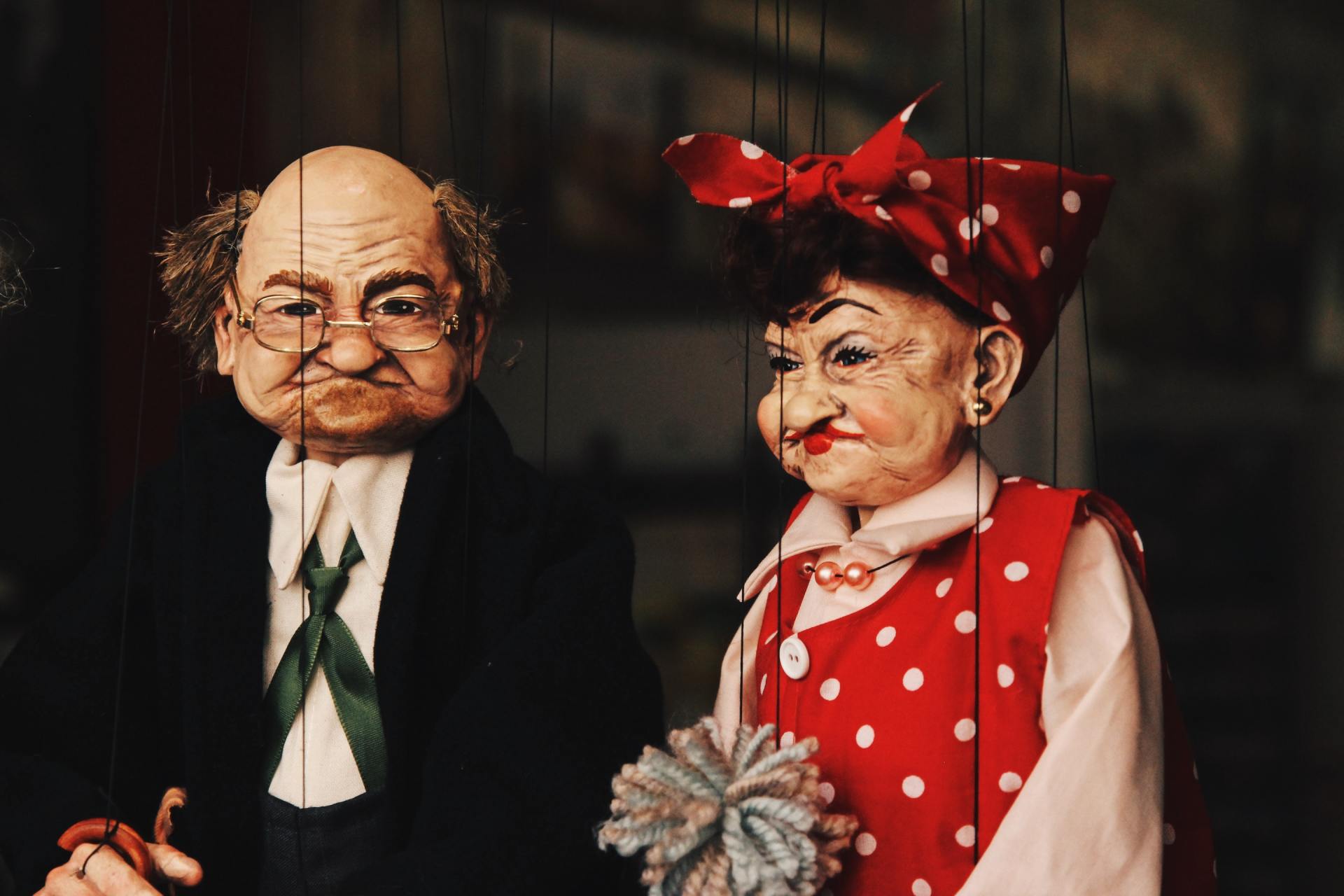 Two puppets with a scowling expression: an older man in a suit, and a woman in a red polka-dot outfit