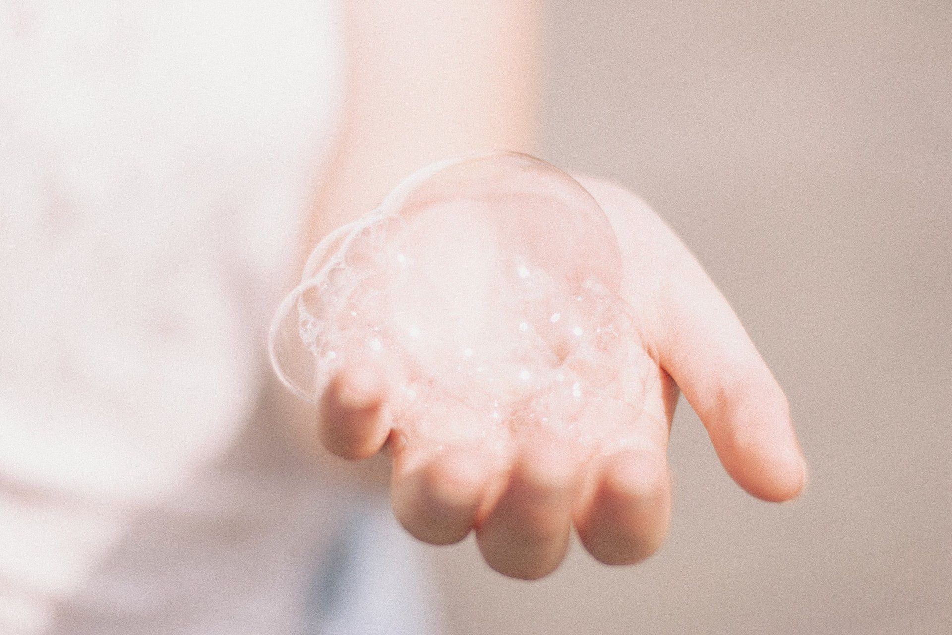 A hand covered in foamy soap being washed under running water