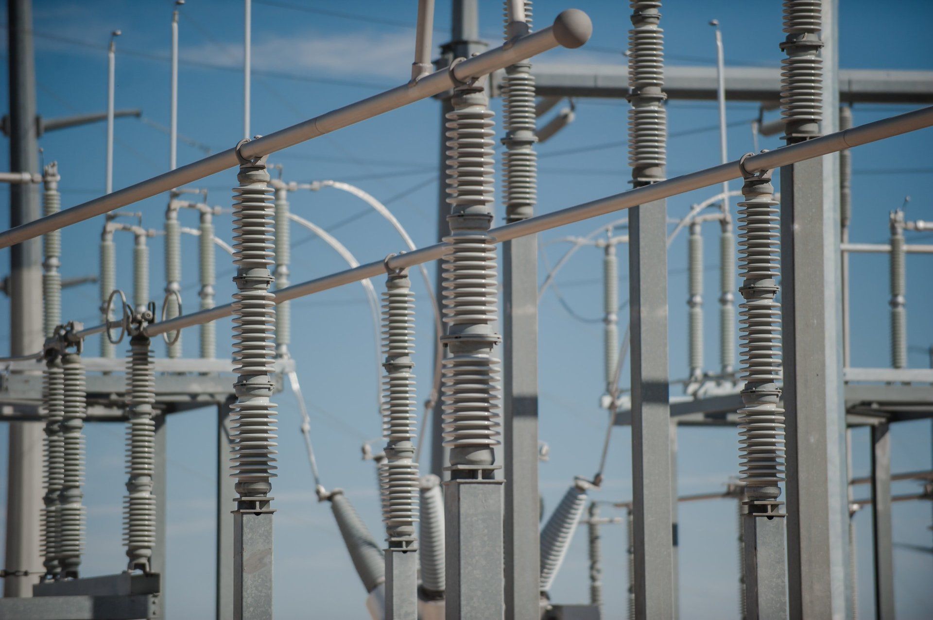 Electrical substation with rows of high-voltage insulators, metal structures, and overhead power lines against a clear blue sky.