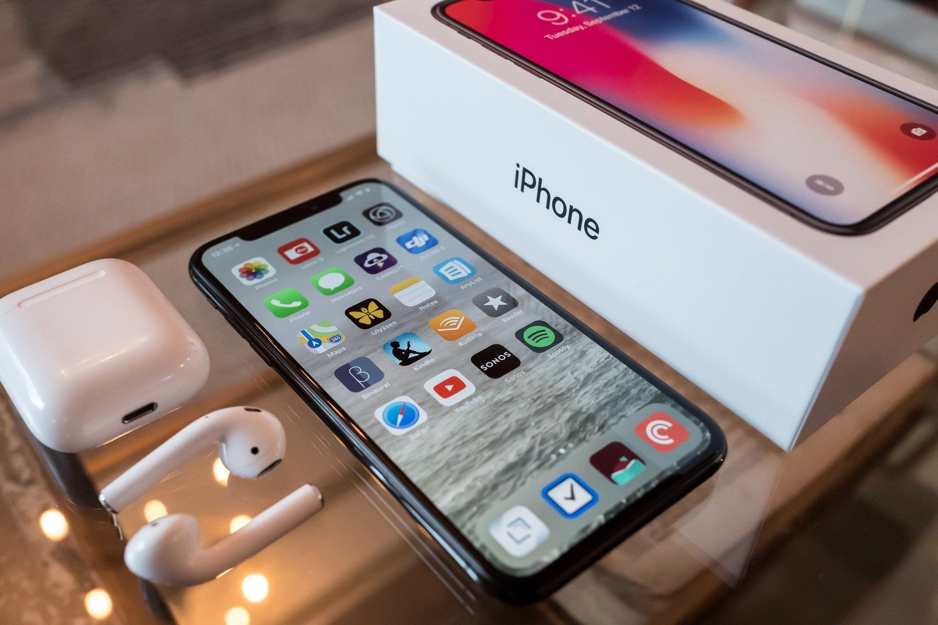 Un iPhone X está sobre una mesa junto a su caja y sus Airpods.