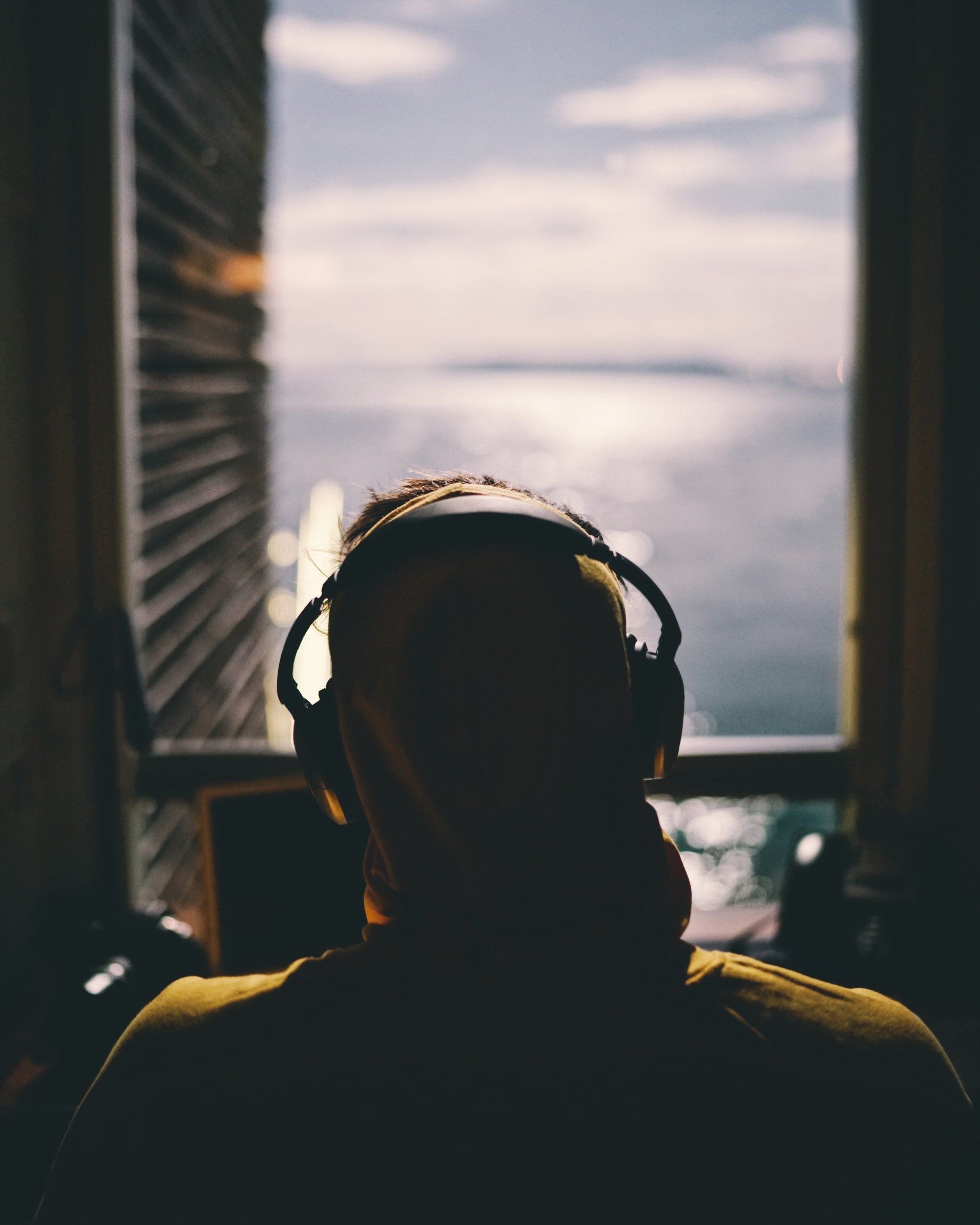 A man wearing headphones looks out a window at the ocean