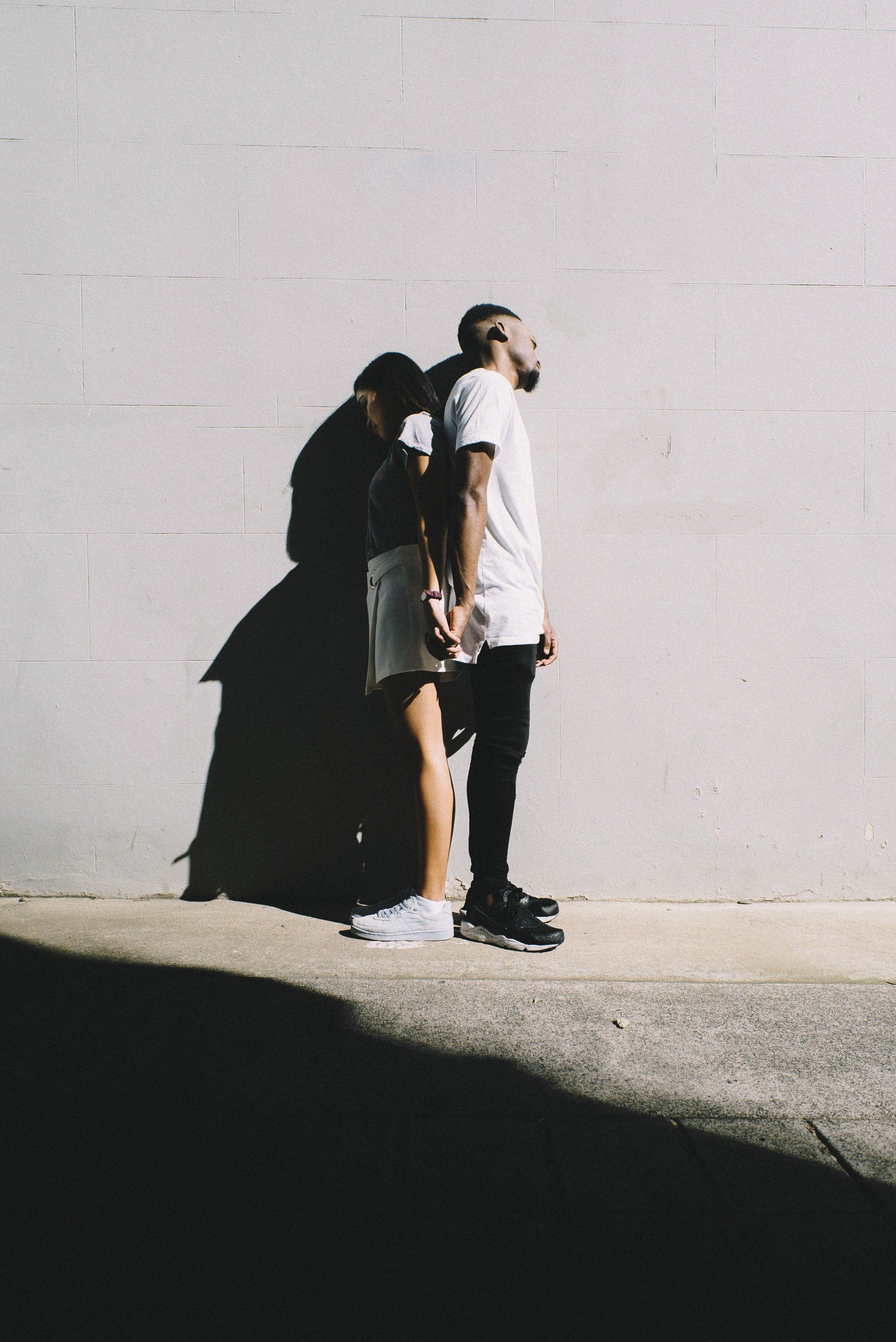 A man and a woman are standing next to each other in front of a white wall.