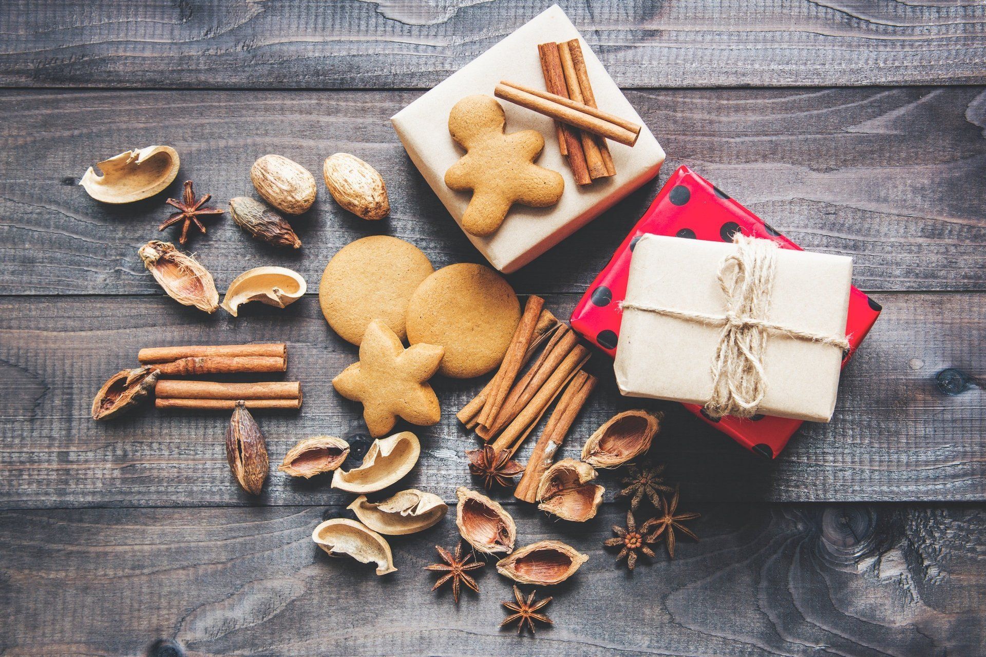 A wooden table topped with gingerbread cookies , cinnamon sticks , star anise and nuts.