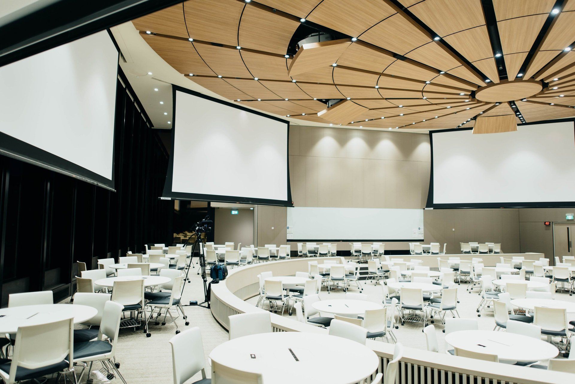 A large conference room with tables and chairs and projector screens