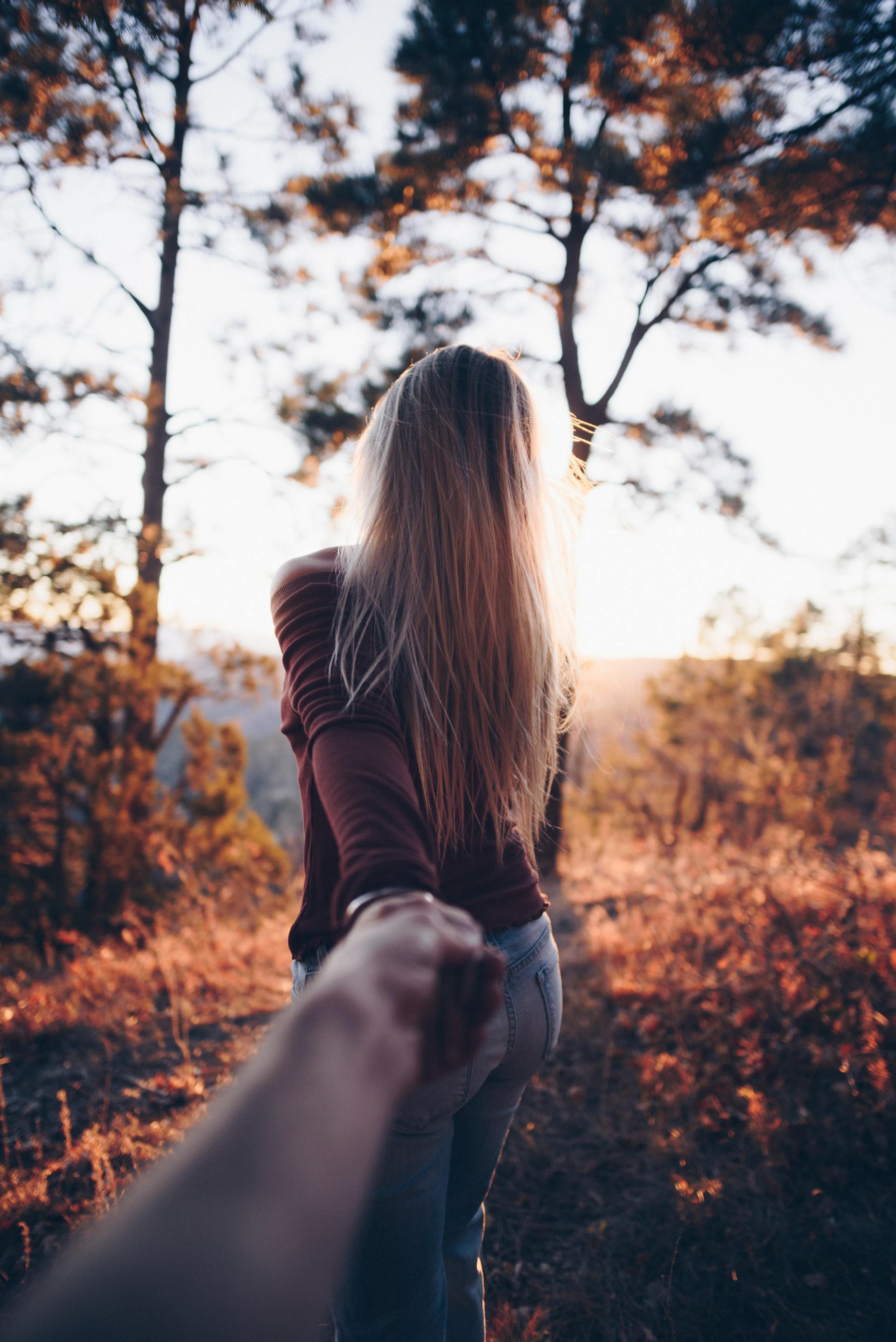 A woman is holding a man 's hand while walking through a forest.